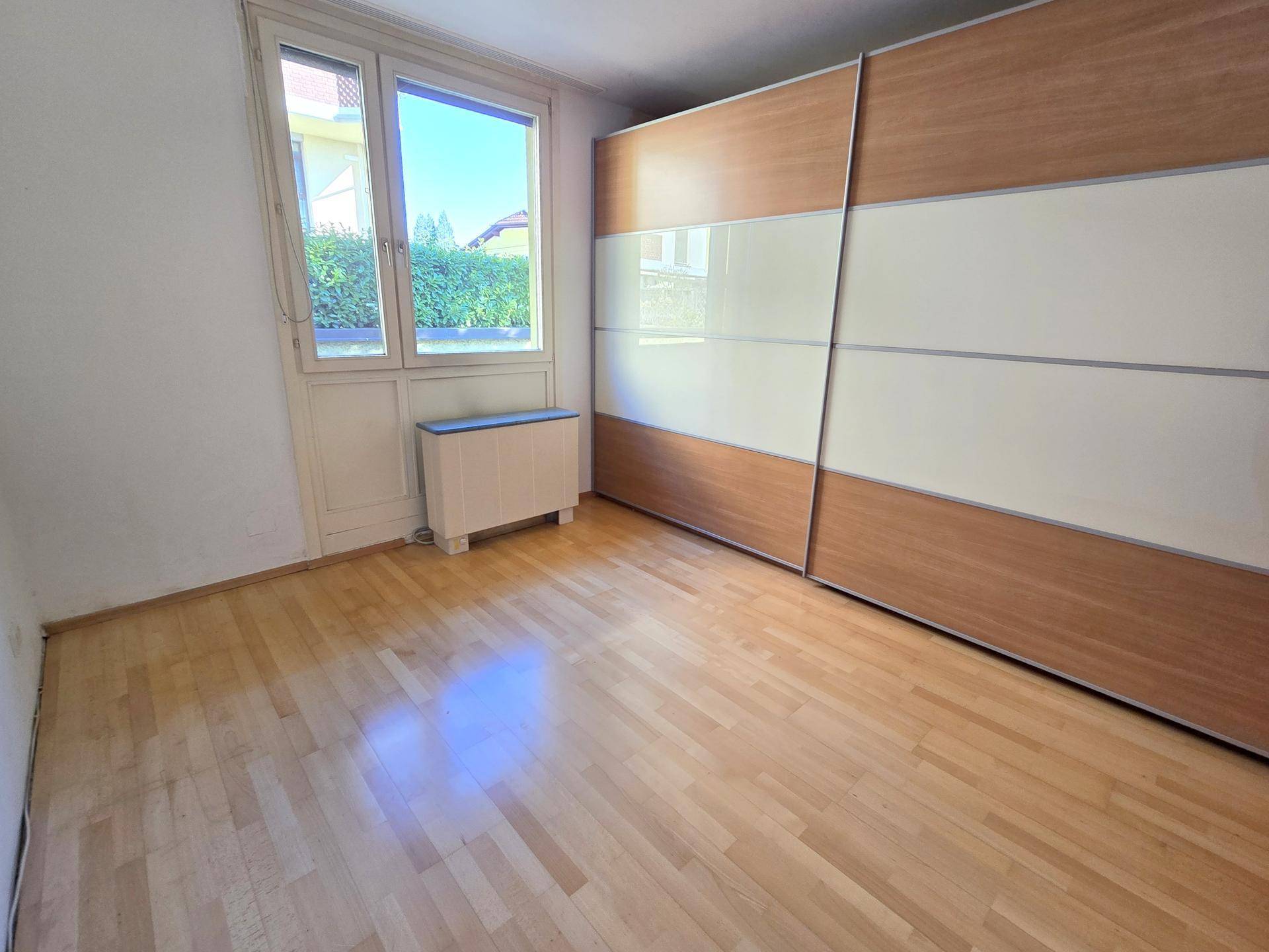 Schlafzimmer mit hellem Parkettboden, großem Fenster und Einbauschrank mit Schiebetüren.