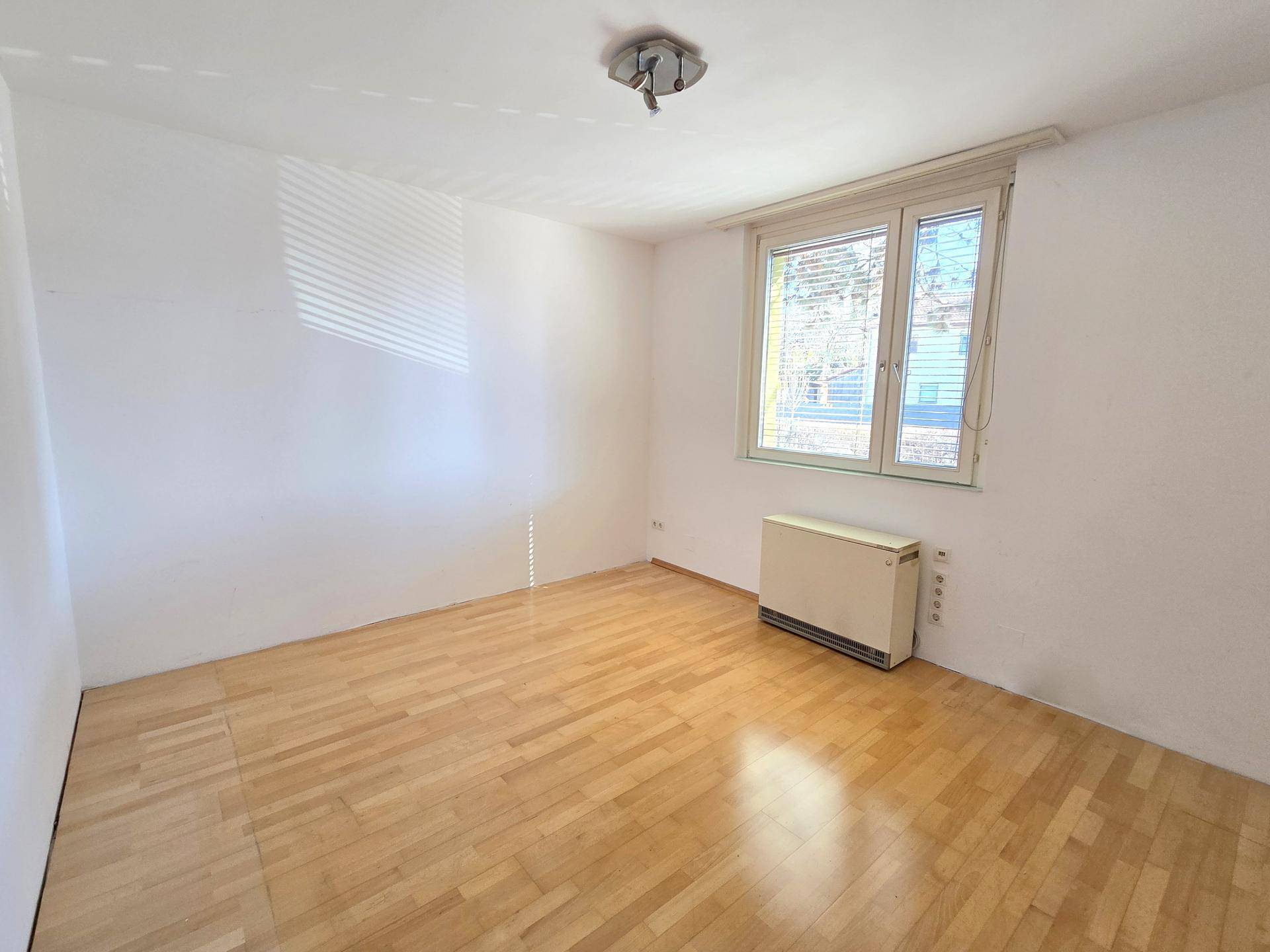 Helles Zimmer mit Parkettboden und großem Fenster, bietet vielseitige Nutzungsmöglichkeiten.