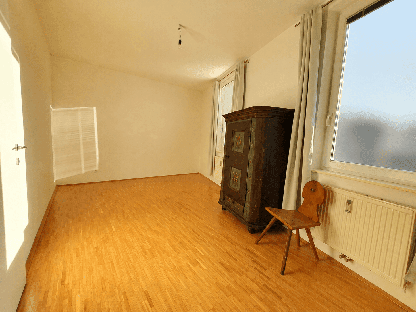 Helles Zimmer mit Parkettboden und traditionellem Holzschrank, viel Tageslicht.