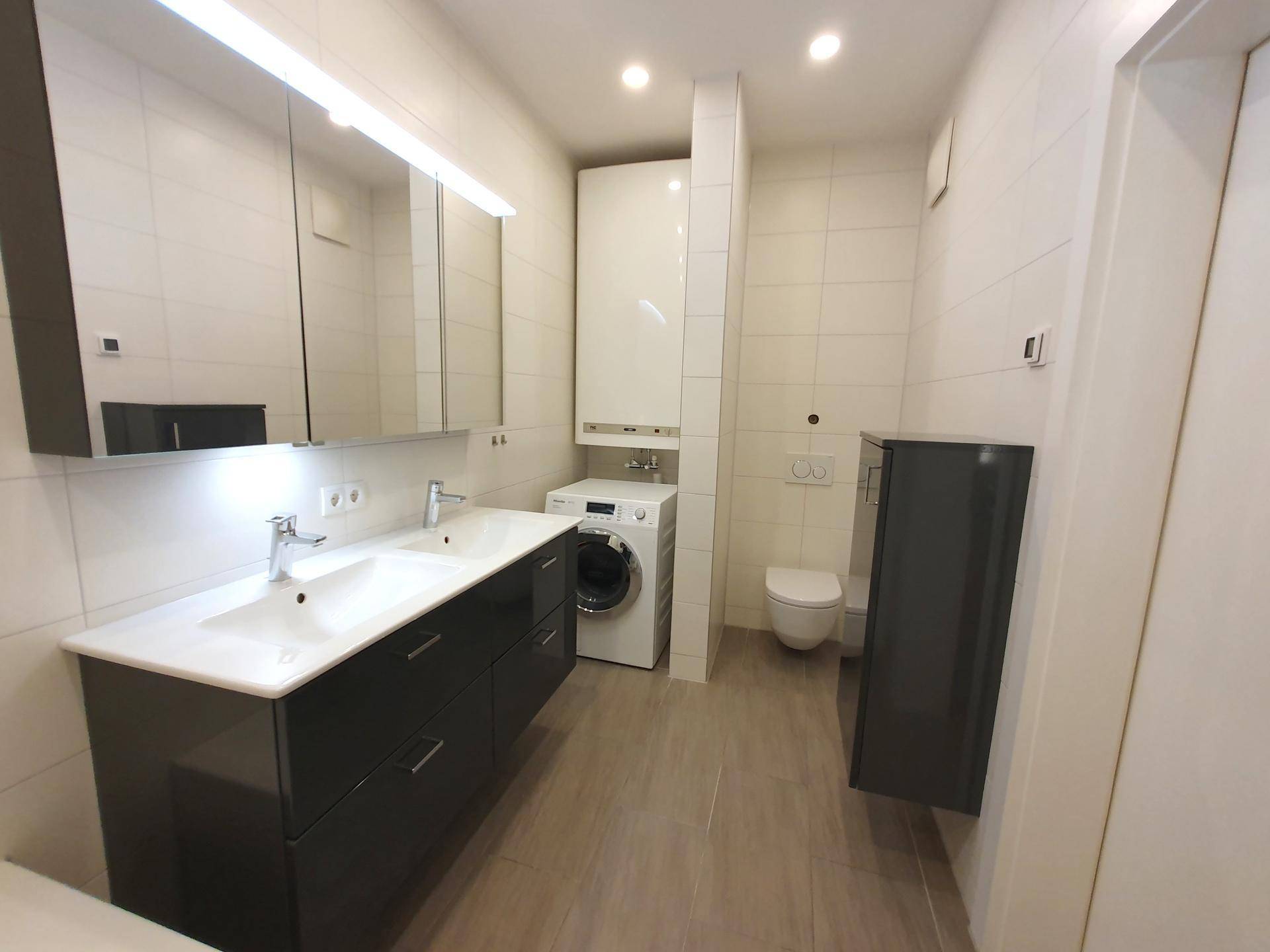 Funktionales Badezimmer mit Doppelwaschbecken, Toilette und Waschmaschinenanschluss.