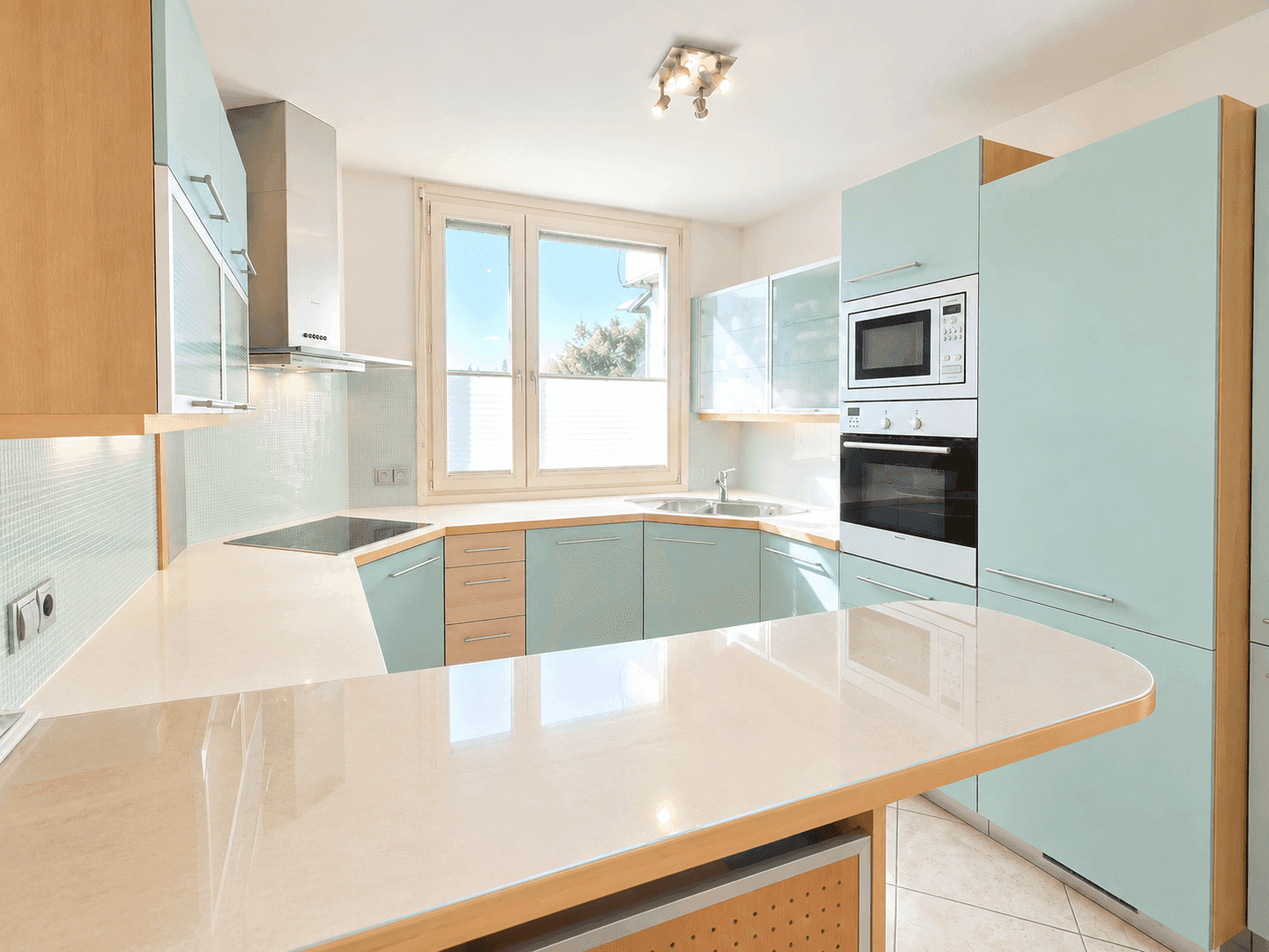 Moderne Einbauküche in Hellblau und Holzoptik mit integrierten Geräten und viel Arbeitsfläche.