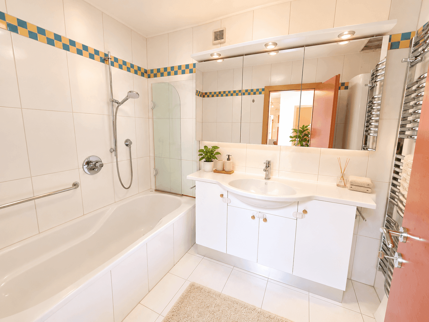 Helles Badezimmer mit Badewanne, Waschtisch und Spiegel, ausgestattet mit weißen Fliesen.