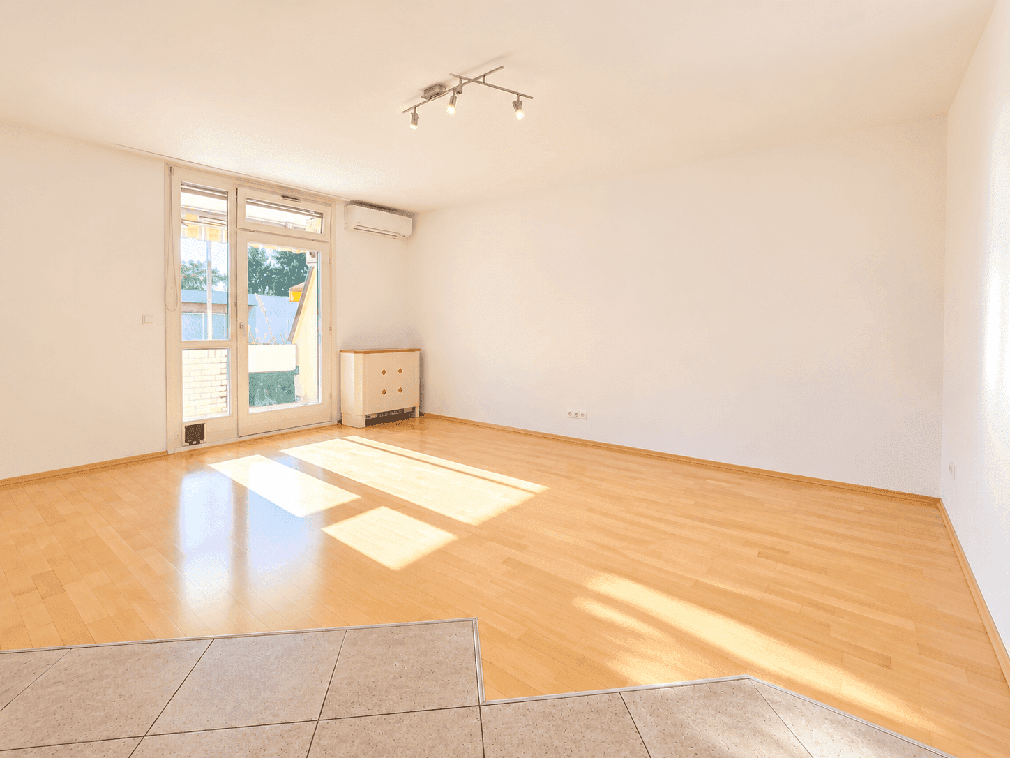 Geräumiges Wohnzimmer mit Parkettboden und Zugang zu einem Außenbereich, hell und einladend.