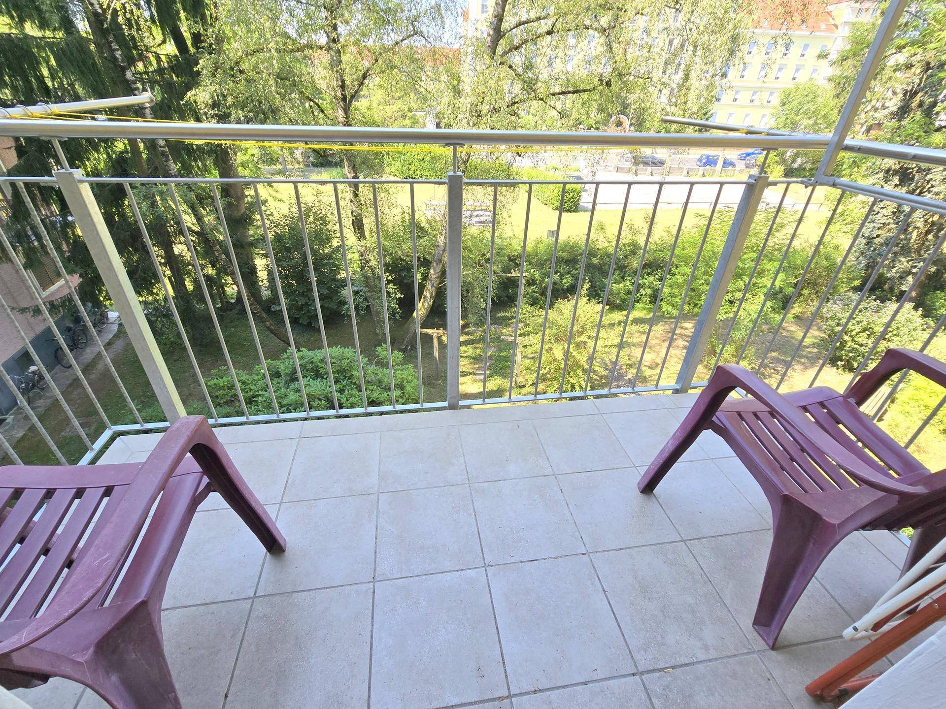 Balkon mit Fliesenboden und Blick ins Grüne, ausgestattet mit Gartenstühlen.