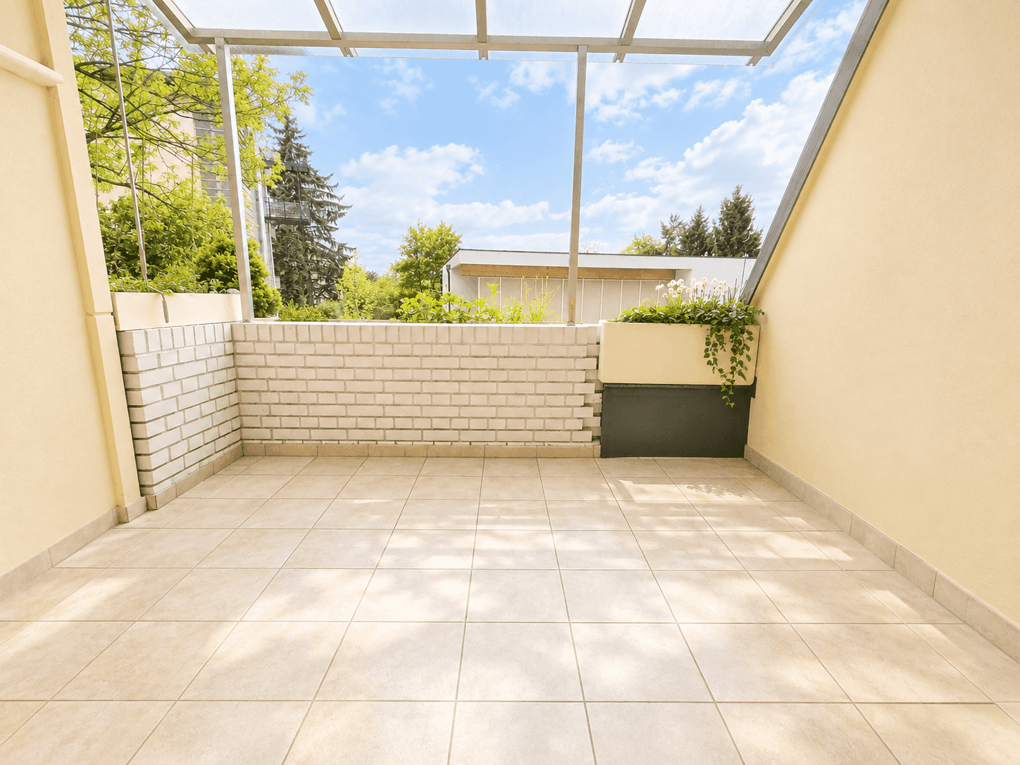 Überdachter Balkon mit Fliesenboden und Blick ins Grüne, ideal für entspannte Stunden.