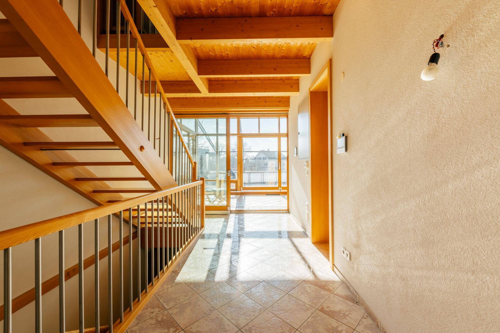 Heller Flur mit Holztreppe, Fliesenboden und großen Fenstern, die den Raum mit Licht füllen.