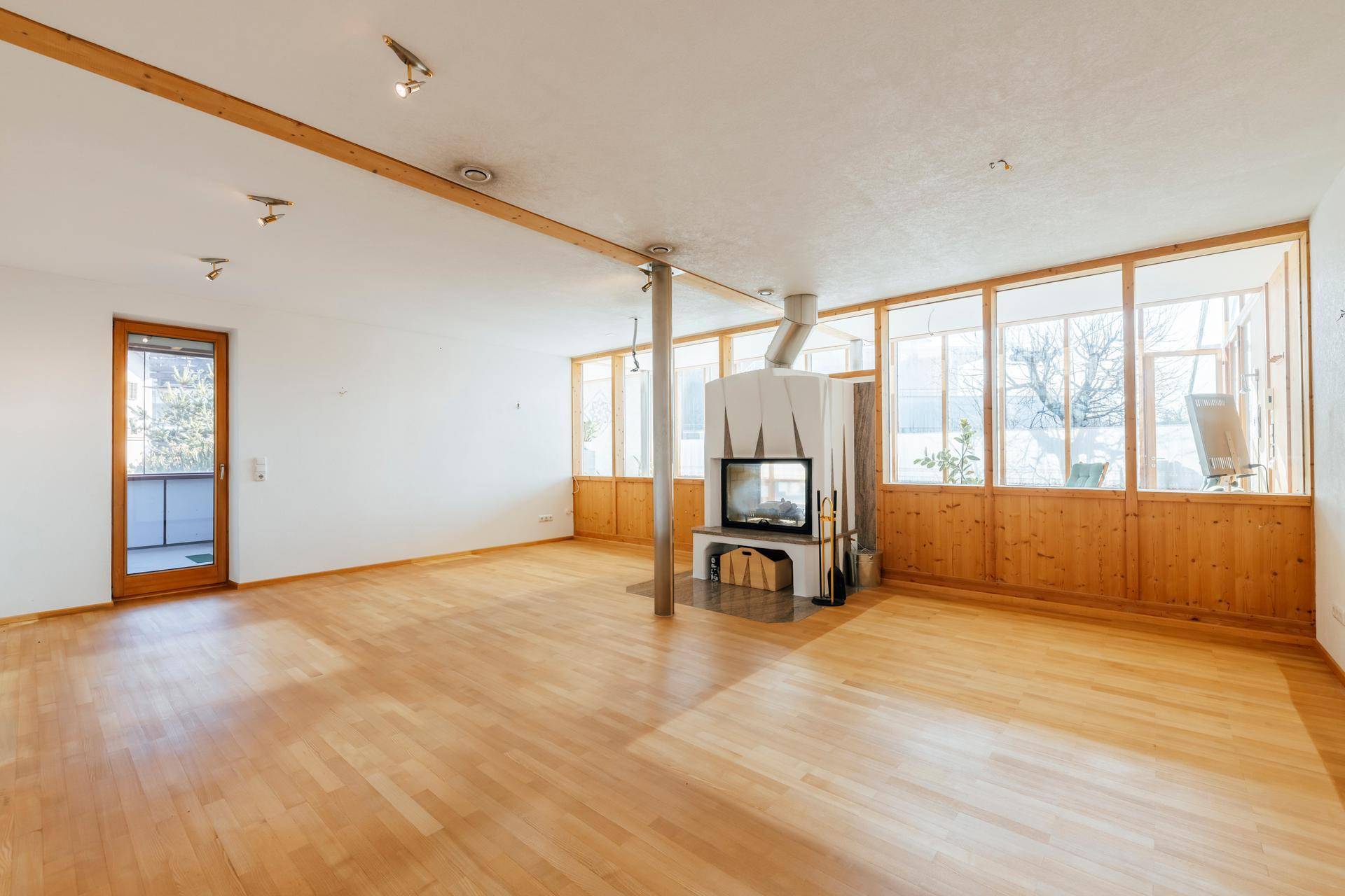 Geräumiges Wohnzimmer mit Holzboden, modernem Kamin und großen Fenstern, die viel Licht hereinlassen.