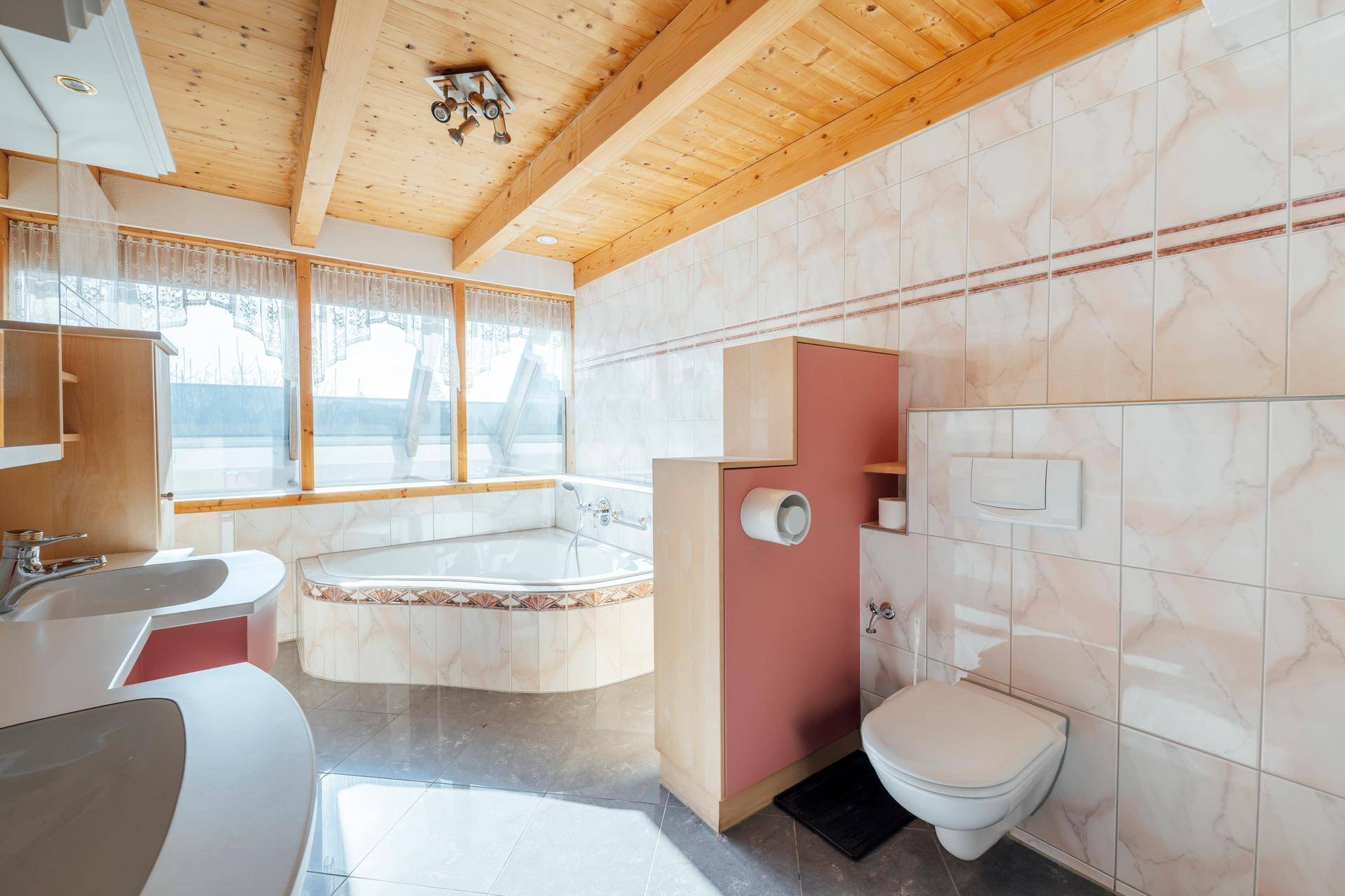 Geräumiges Badezimmer mit Eckbadewanne, WC, Waschbecken und Holzbalkendecke.
