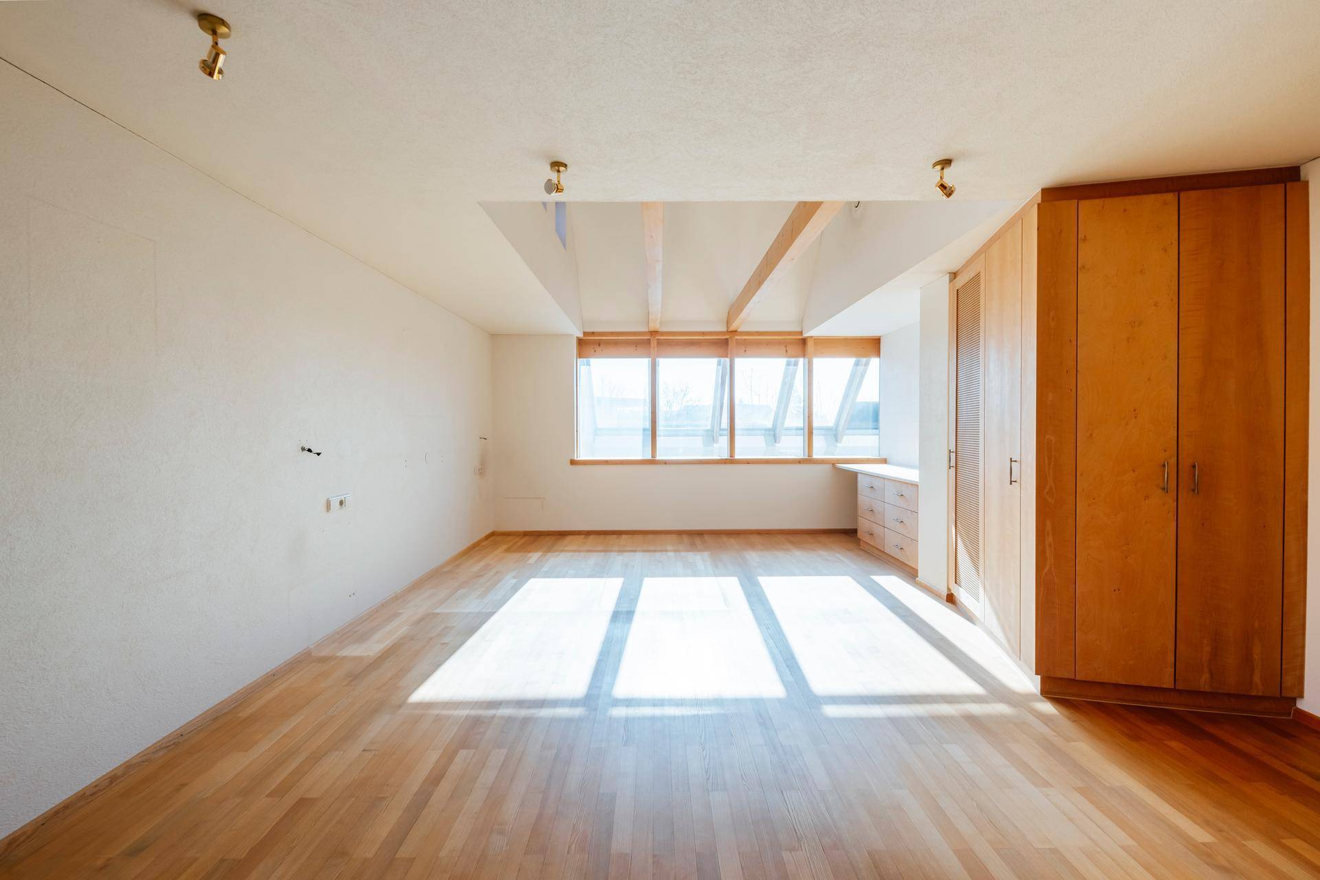 Helles Schlafzimmer mit Holzboden, Einbauschränken und großen Fenstern, die den Raum sonnig machen.