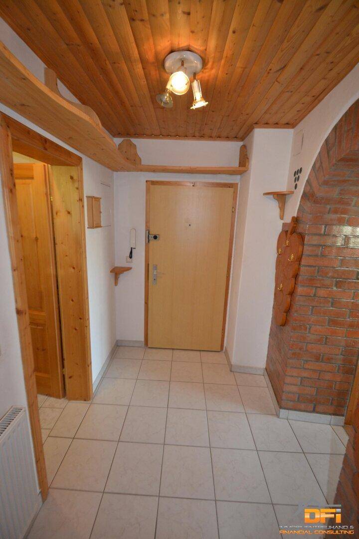 Eingangsbereich mit Fliesenboden, Holzdecke, Ziegelbogen und Holztür.