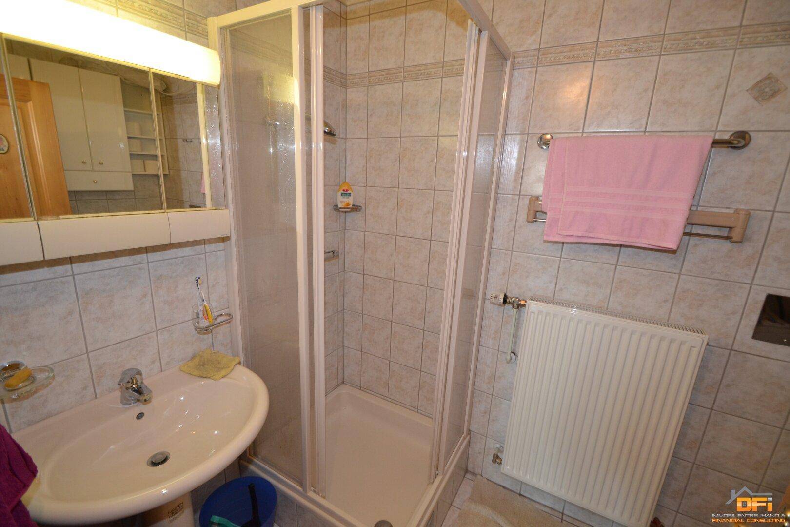 Badezimmer mit Duschkabine, Waschbecken und hellen Wand- und Bodenfliesen.