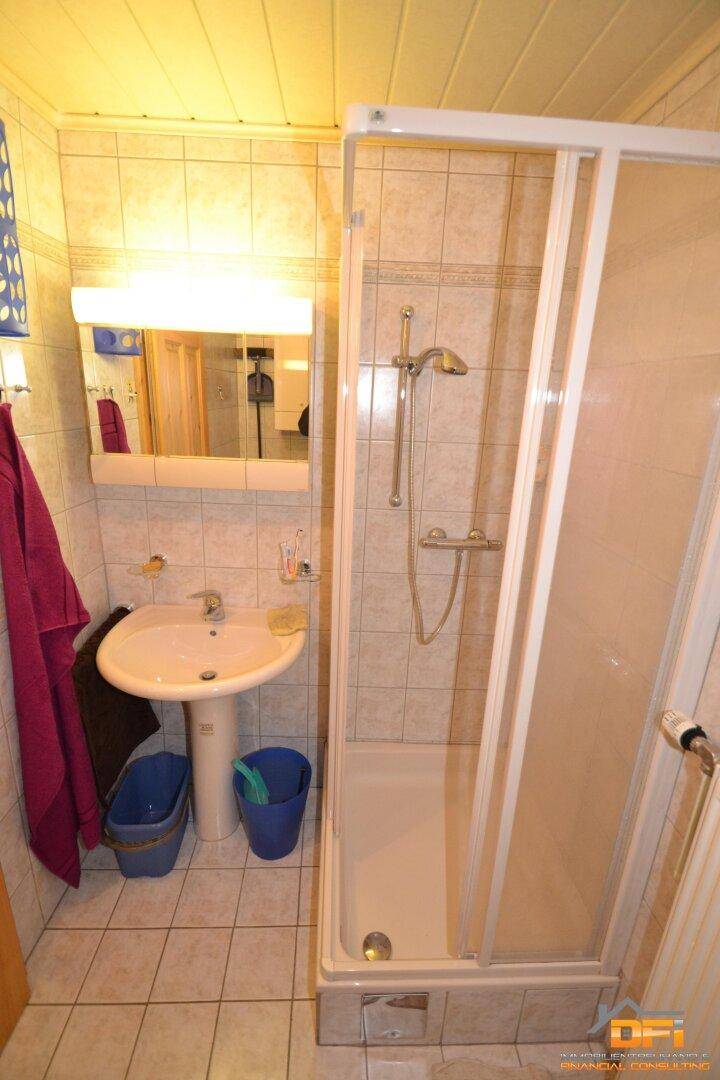 Badezimmer mit Duschkabine, Waschbecken, Spiegelschrank und Heizkörper.