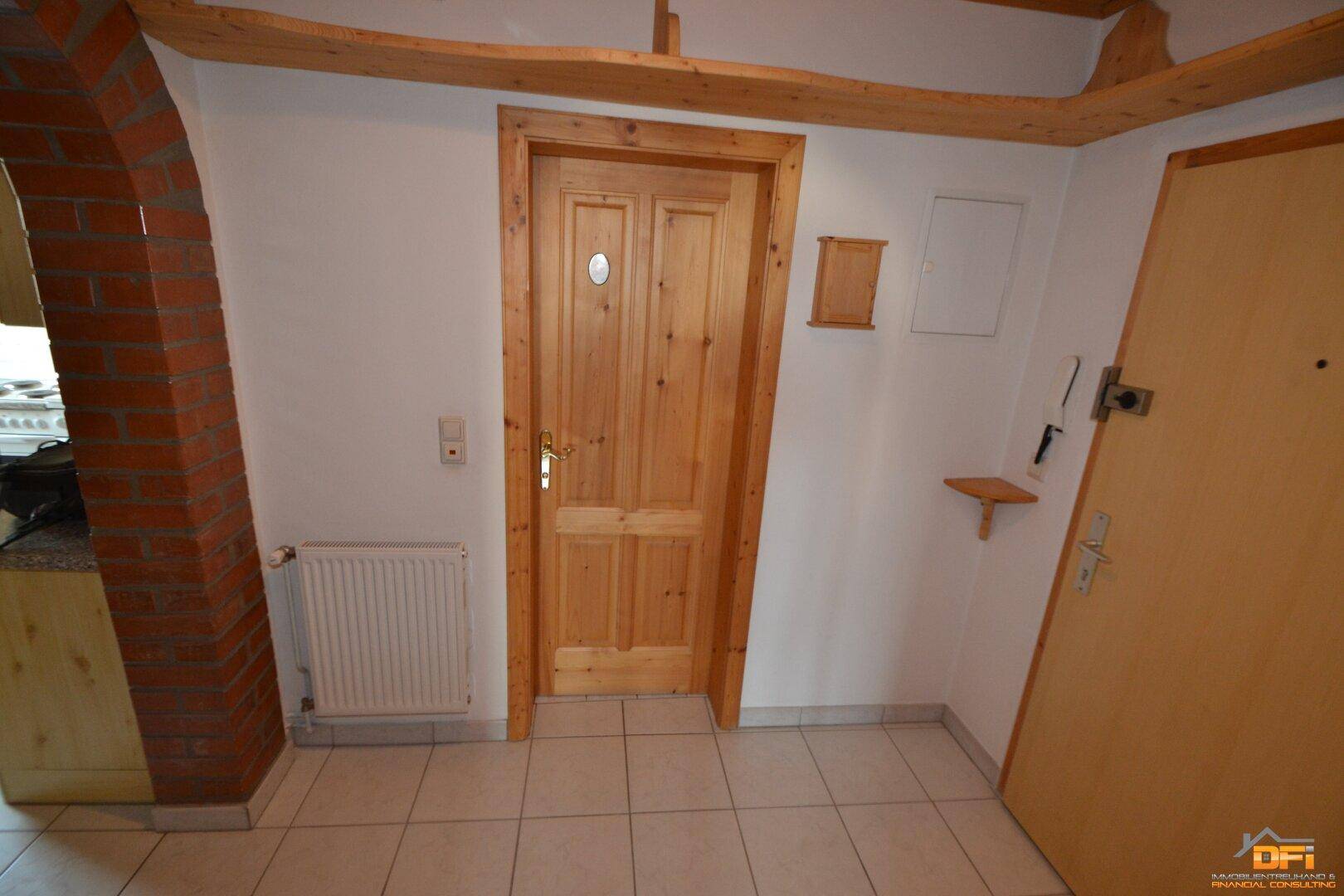 Eingangsbereich mit Holztür, Fliesenboden und Heizkörper.