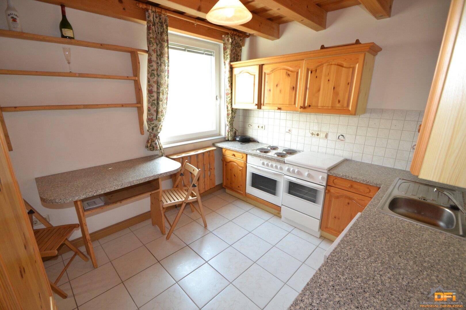 Küche im Landhausstil mit Holzschränken, Fliesenboden und Essbereich am Fenster.