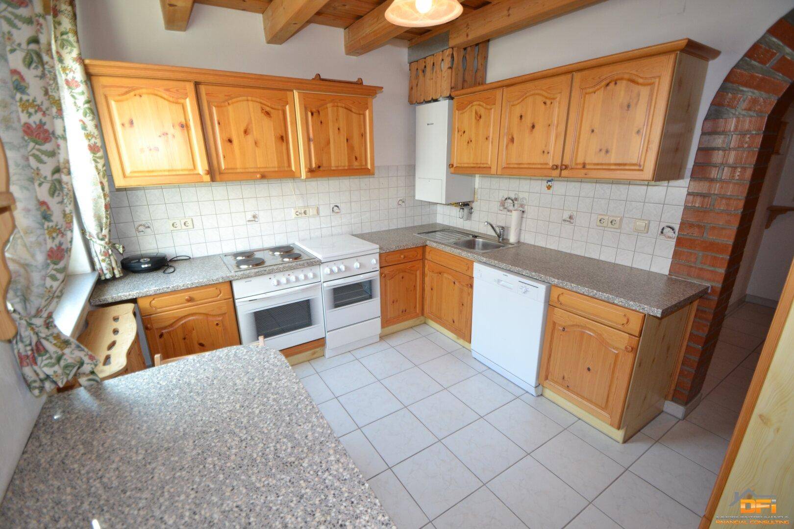 Funktionale Küche mit Holzschränken, Fliesenboden und integrierten Geräten.