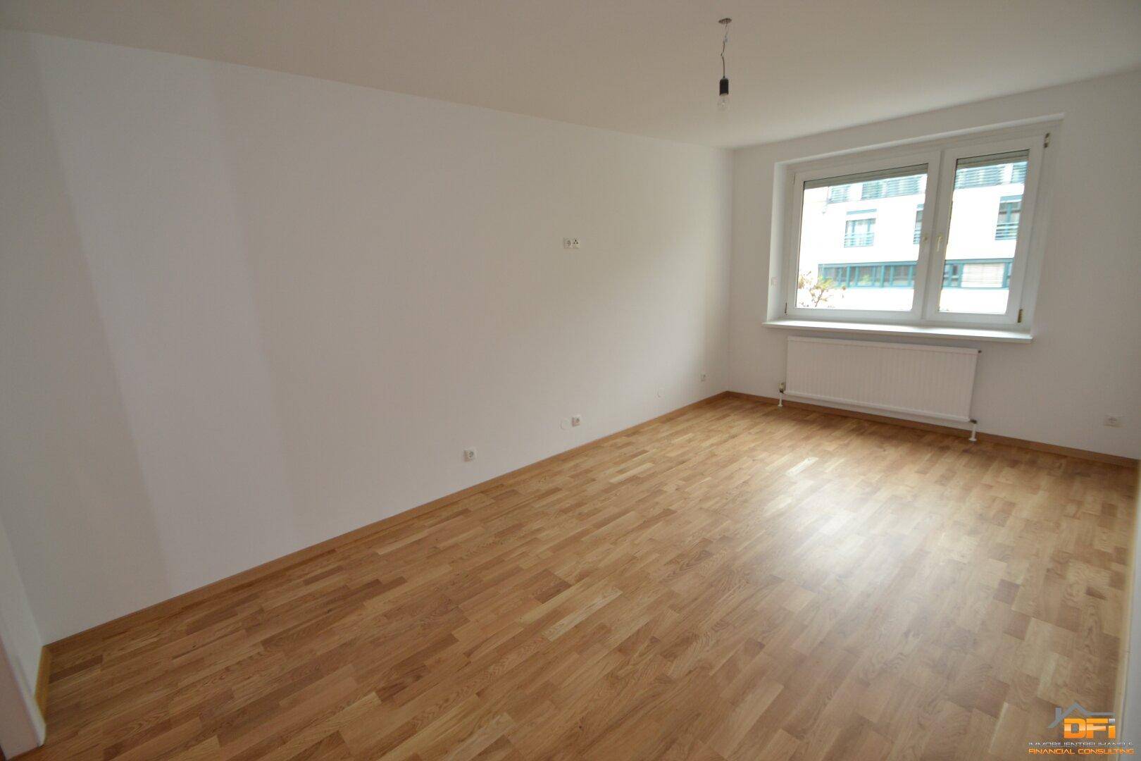 Leeres Schlafzimmer mit hellem Parkettboden und einem Fenster, das viel Tageslicht hereinlässt.