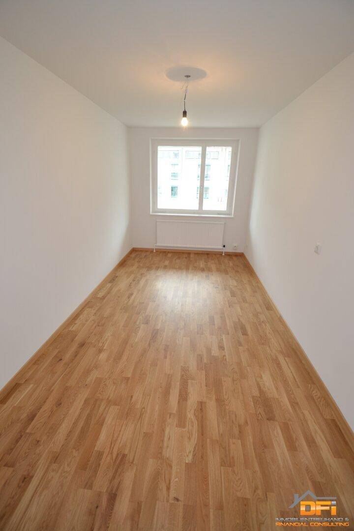 Schmales Schlafzimmer mit hellem Parkettboden und Fenster, ideal als Kinder- oder Arbeitszimmer.