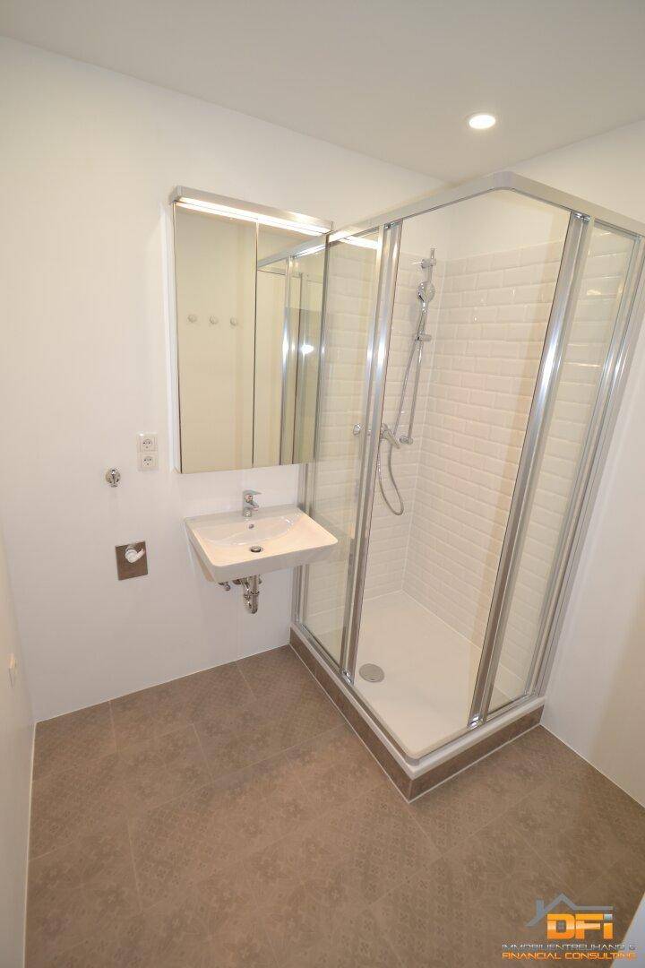 Modernes Badezimmer mit Duschkabine, Einzelwaschbecken und hellen Fliesen an Wand und Boden.