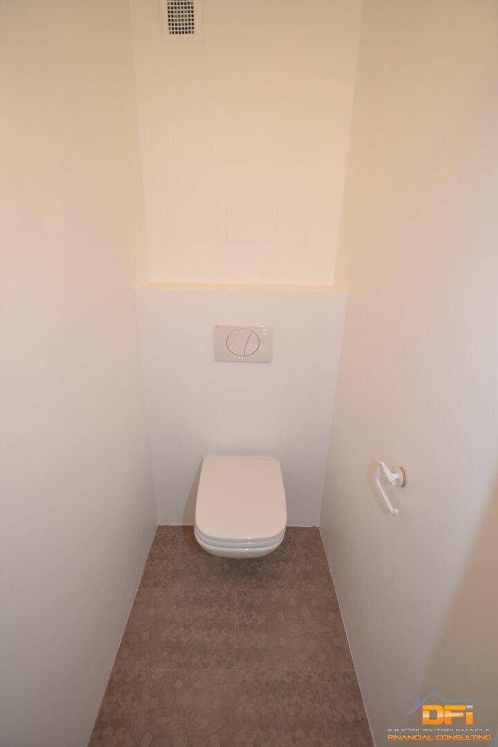 Separates WC mit wandhängender Toilette und Fliesenboden, ausgestattet mit Abluftventilator.