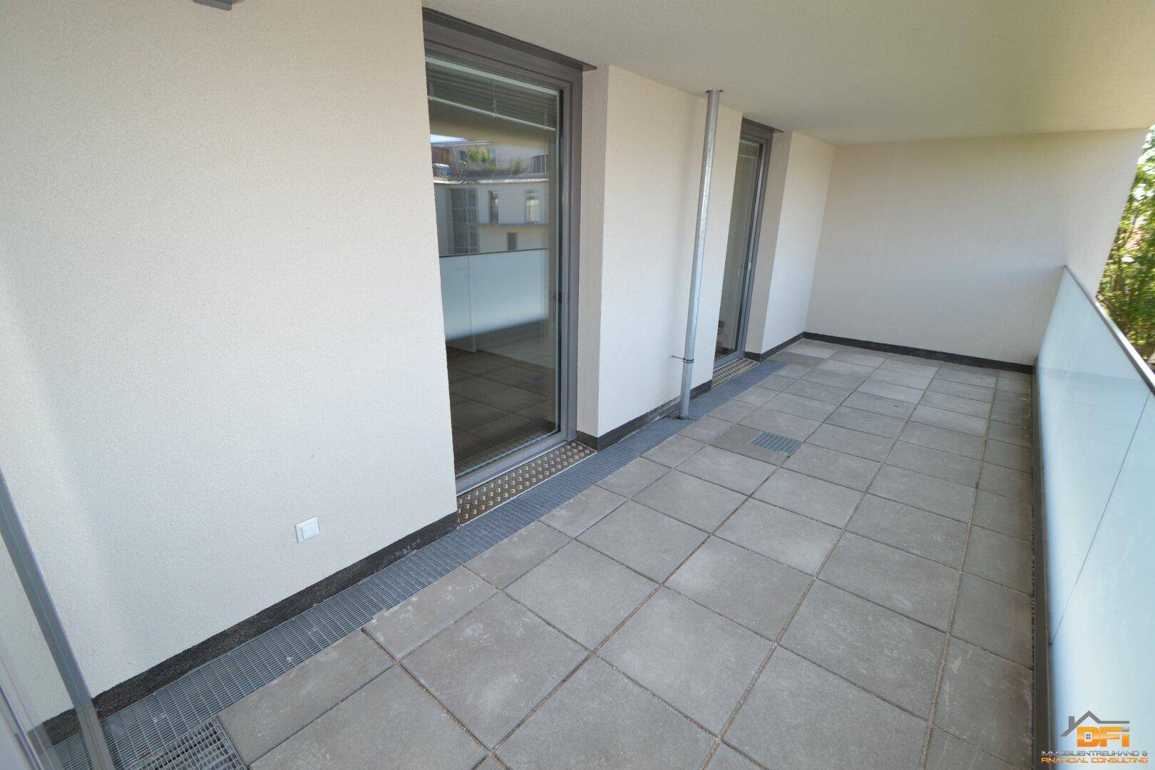 Geräumiger Balkon mit Fliesenboden und moderner Glasbrüstung, ideal für Entspannung im Freien.