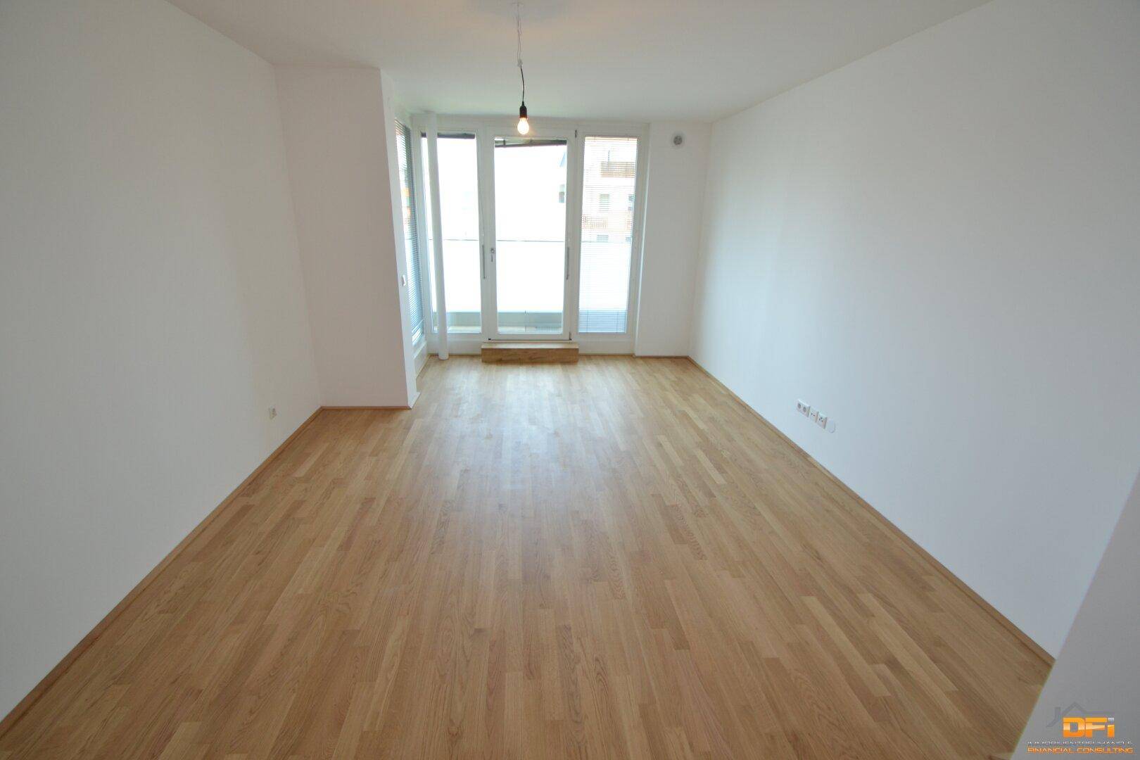 Heller Raum mit Parkettboden und Zugang zu einem Balkon, bietet viel natürliches Licht.
