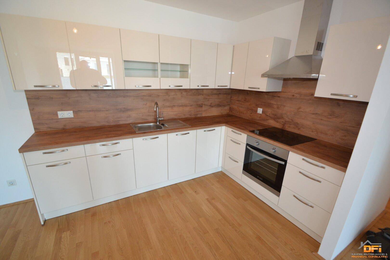 Moderne Einbauküche mit weißen Hochglanzfronten, Holzoptik-Arbeitsplatte und integrierten Geräten.