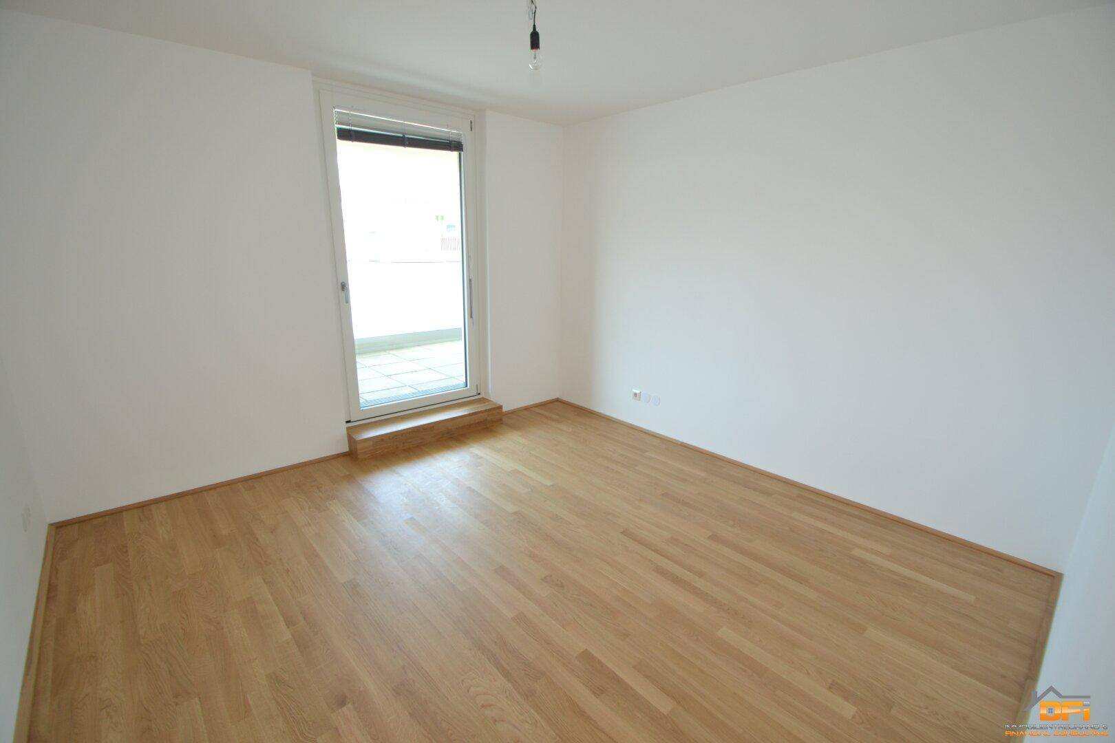 Helles Schlafzimmer mit Parkettboden und Zugang zu einem Balkon, bietet viel Tageslicht.