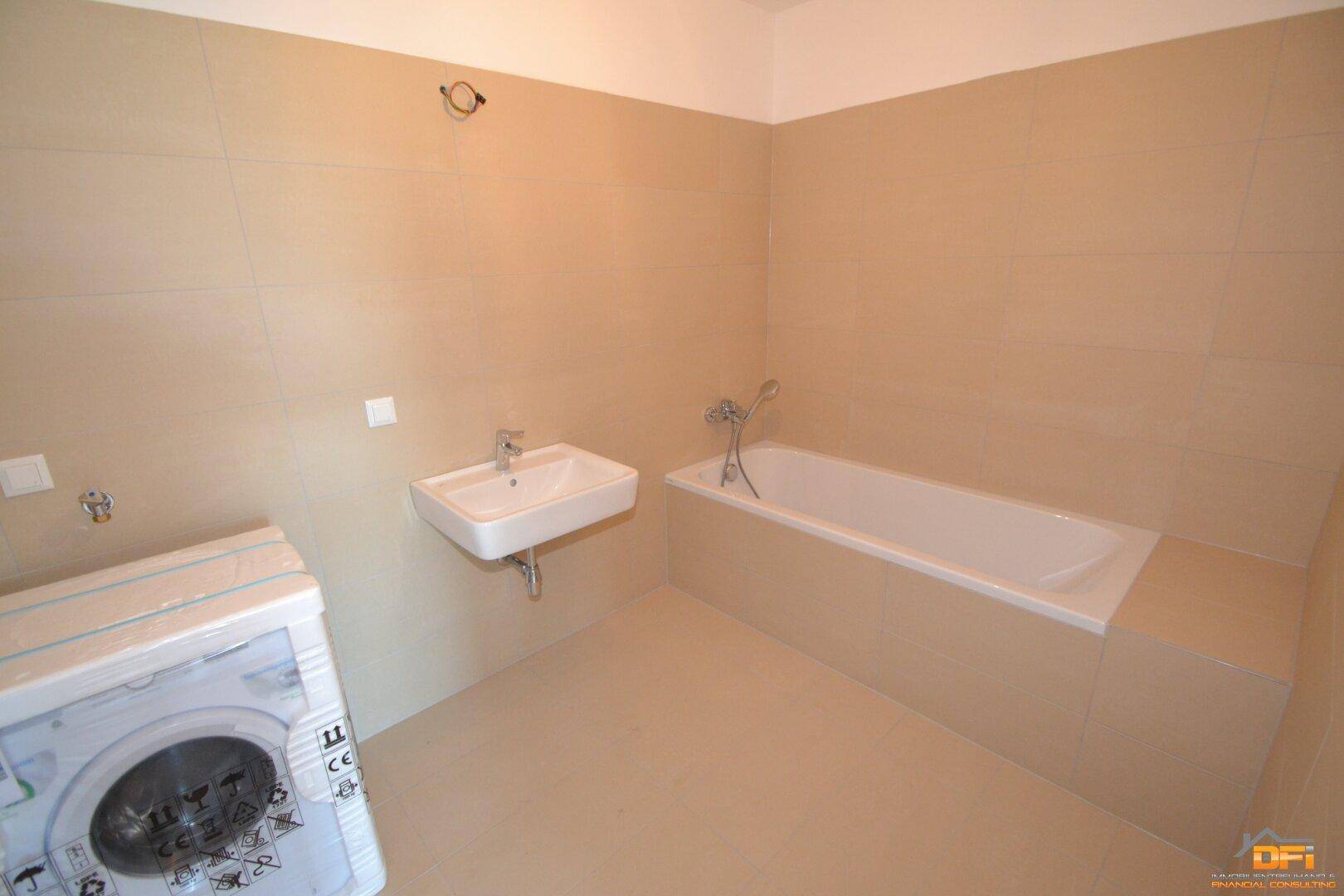 Geräumiges Badezimmer mit Badewanne, Waschbecken und beigefarbenen Fliesen.