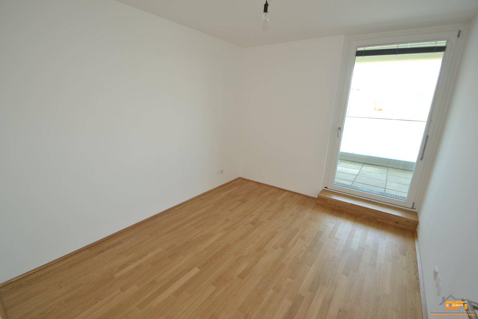 Helles Schlafzimmer mit Parkettboden und Zugang zu einem Balkon, ideal für natürliches Licht.
