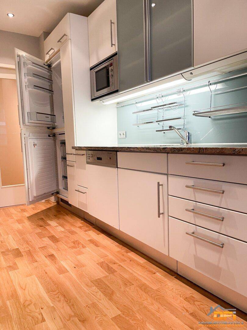 Moderne Küche mit weißen Schränken, Granitarbeitsplatte und integrierten Geräten wie Kühlschrank und Geschirrspüler.