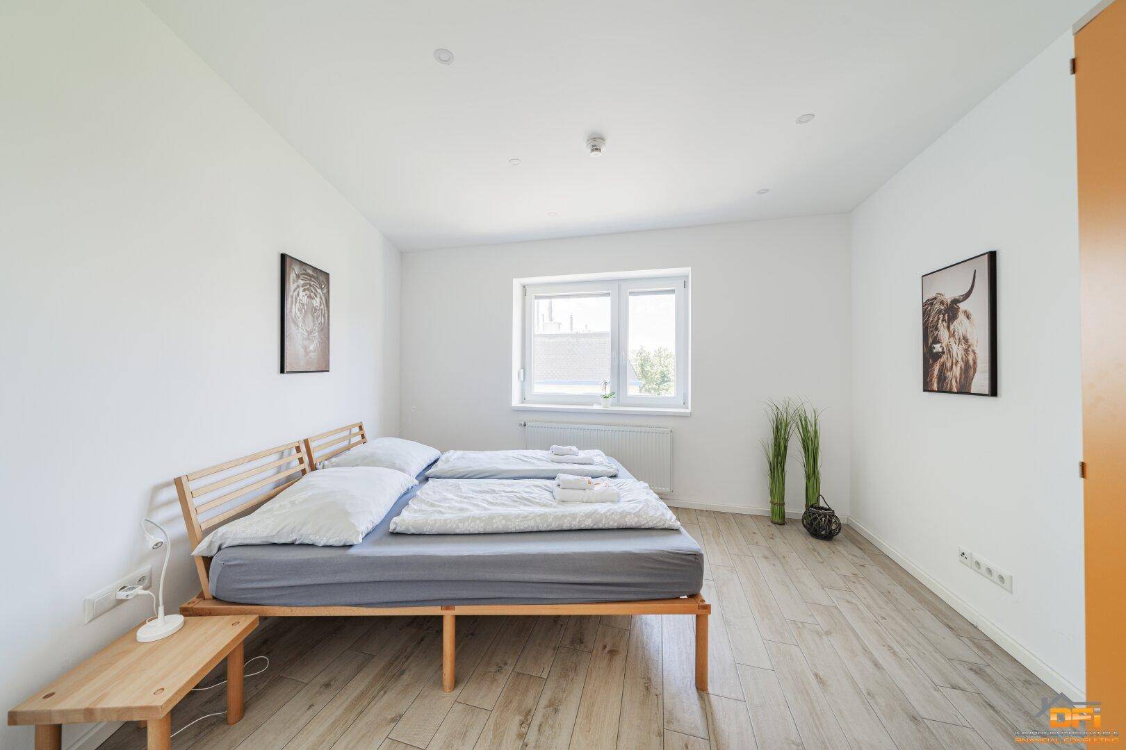 Helles Schlafzimmer mit Doppelbett, Holzrahmen und Laminatboden, gut beleuchtet durch ein Fenster.