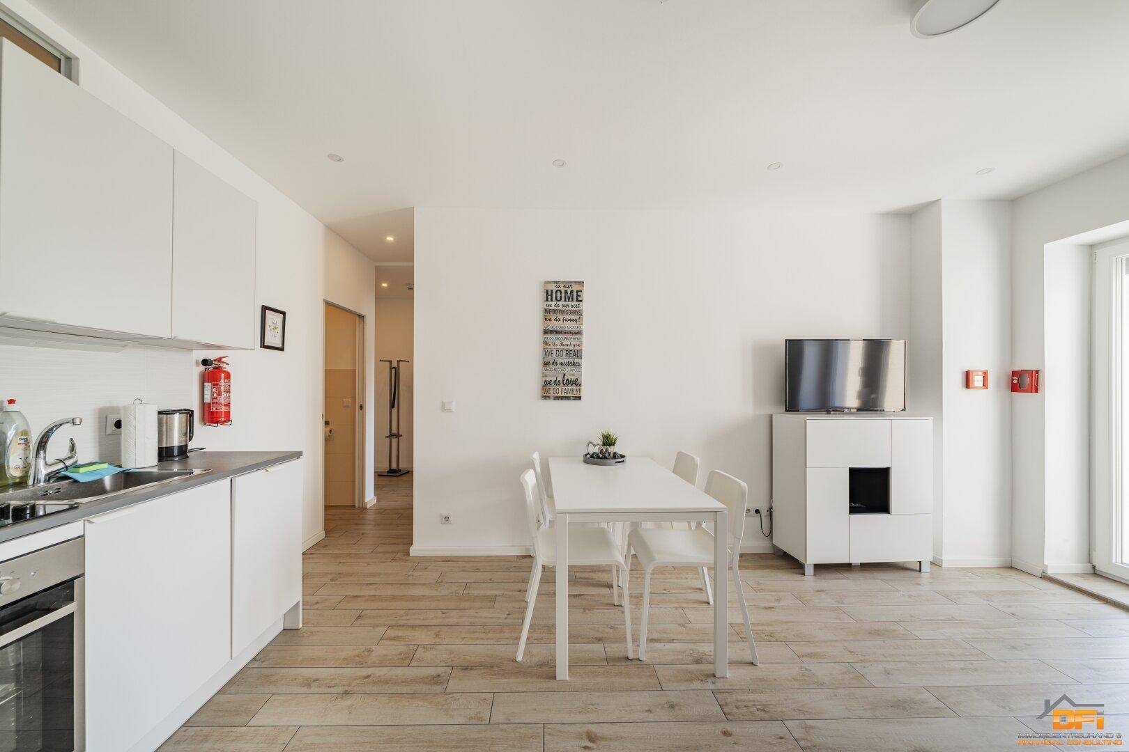 Offener Wohnbereich mit integrierter Küche, Esstisch und Zugang zum Balkon.