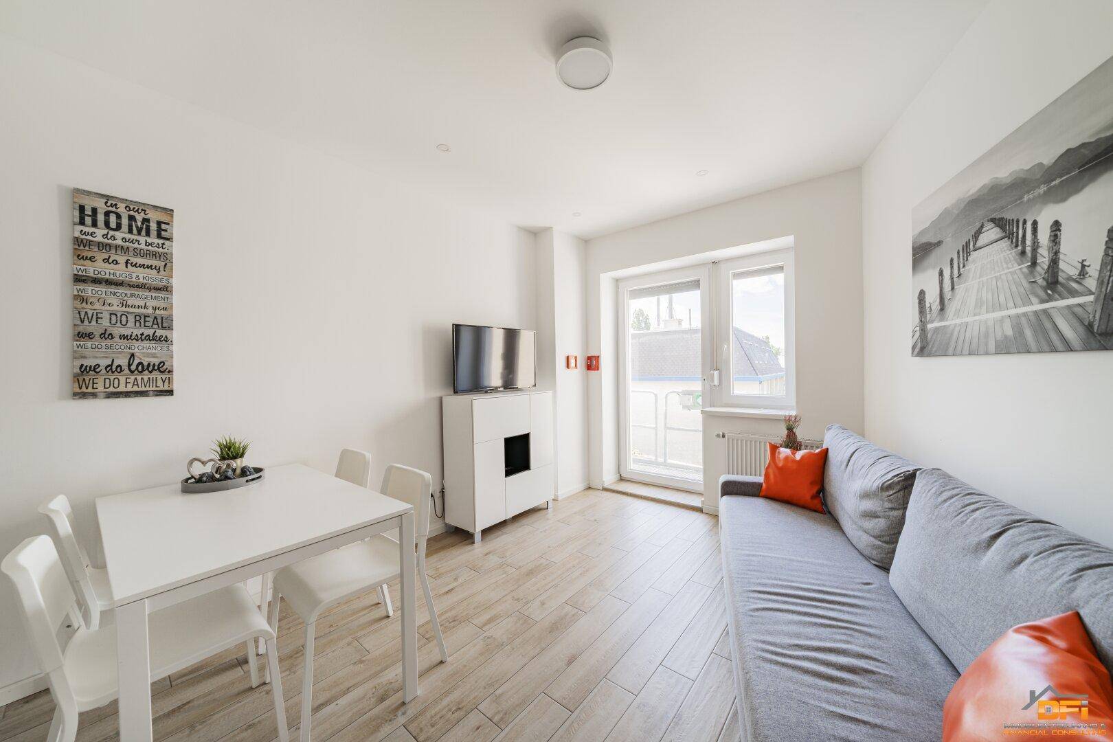 Helles Wohn- und Esszimmer mit grauem Sofa, weißem Esstisch und Balkonzugang.