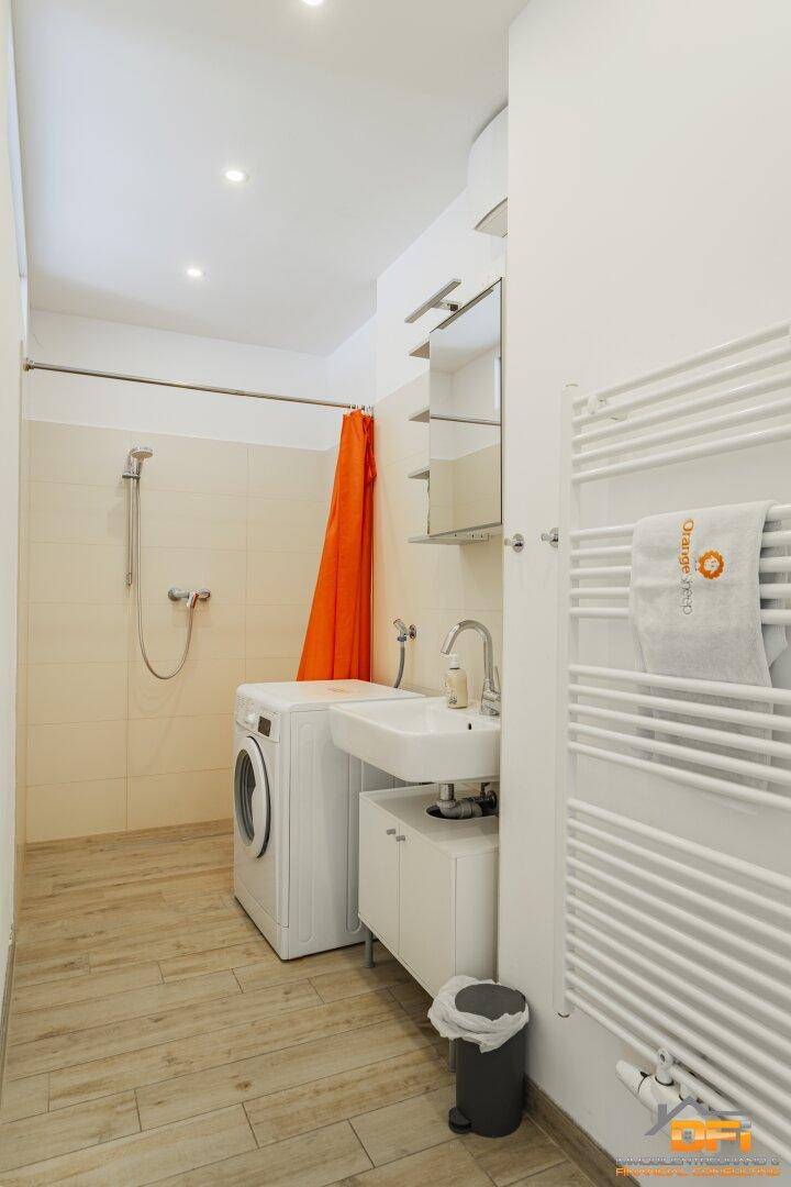 Helles Badezimmer mit Dusche, Waschbecken, Waschmaschine und WC, ausgestattet mit modernen Fliesen.