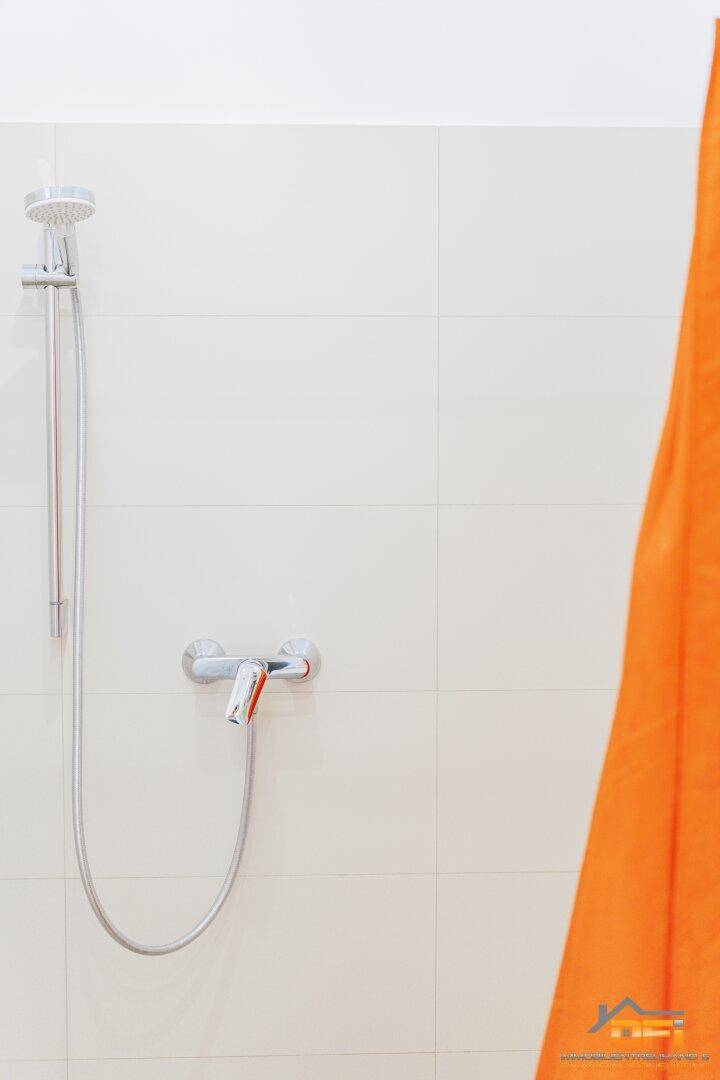 Nahaufnahme des Duschkopfs und der Armatur im gefliesten Duschbereich des Badezimmers.