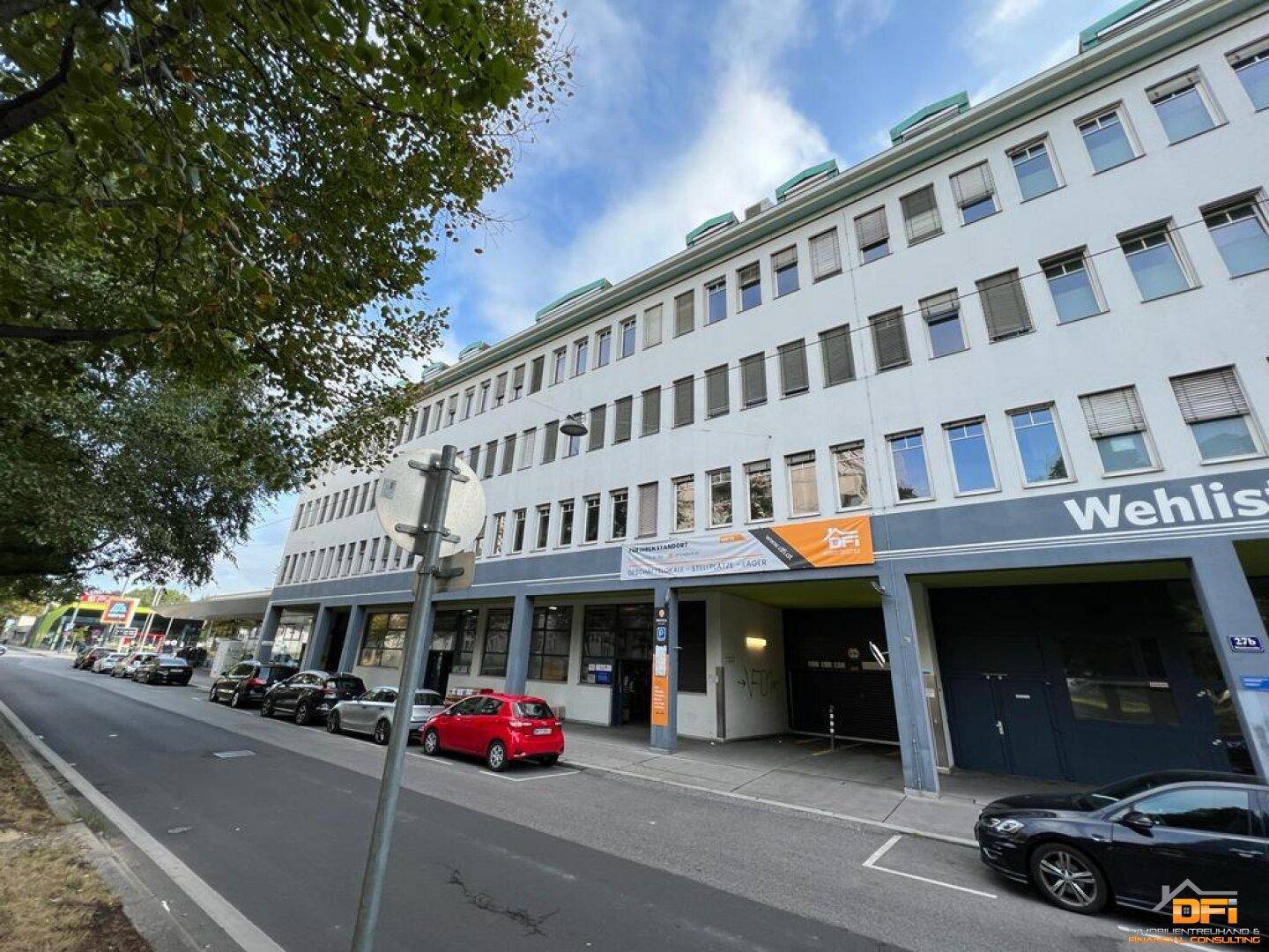Mehrstöckiges Geschäftsgebäude mit zahlreichen Fenstern und Parkplätzen entlang der Straße.