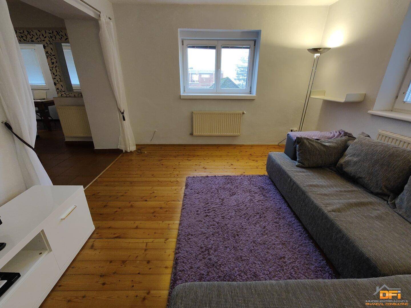 Gemütliches Wohnzimmer mit Holzboden, Sofa und Fenster mit Blick nach draußen unter Dachschräge.