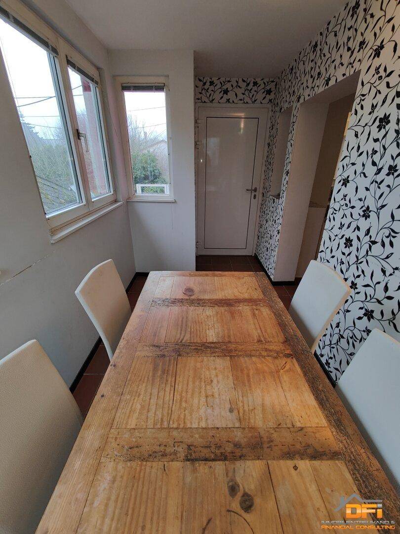 Essbereich mit großem Holztisch, floraler Tapete und Fenstern mit Außenblick.