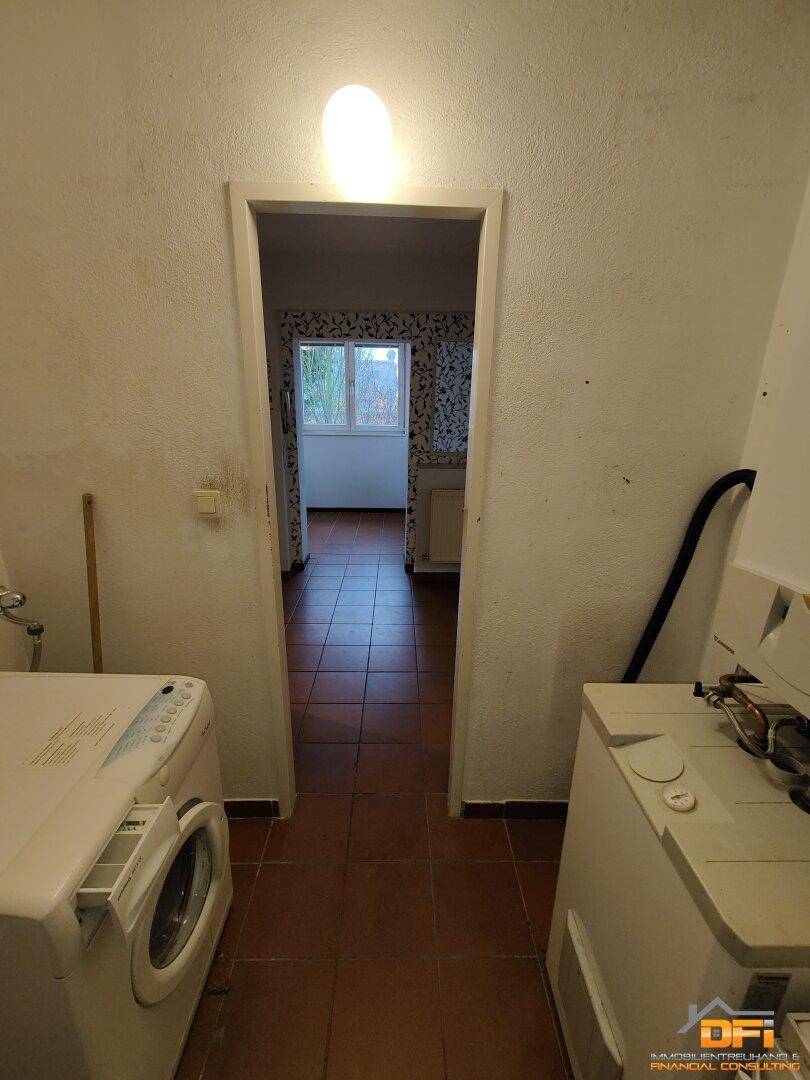 Hauswirtschaftsraum mit Waschmaschine und Zugang zu einem weiteren Raum.