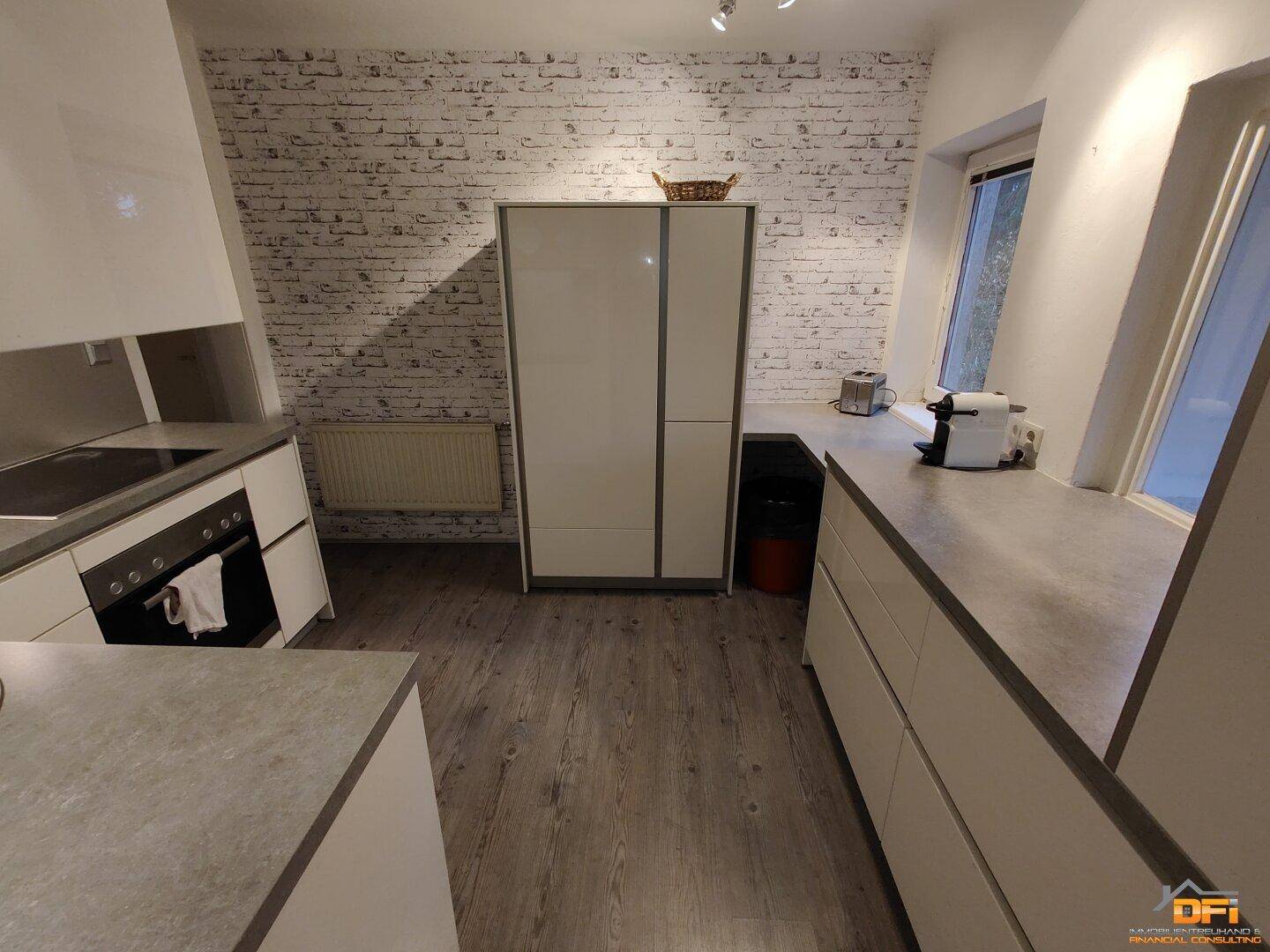 Moderne Küche mit weißen Schränken, Backsteinwand und Arbeitsflächen auf Laminatboden.