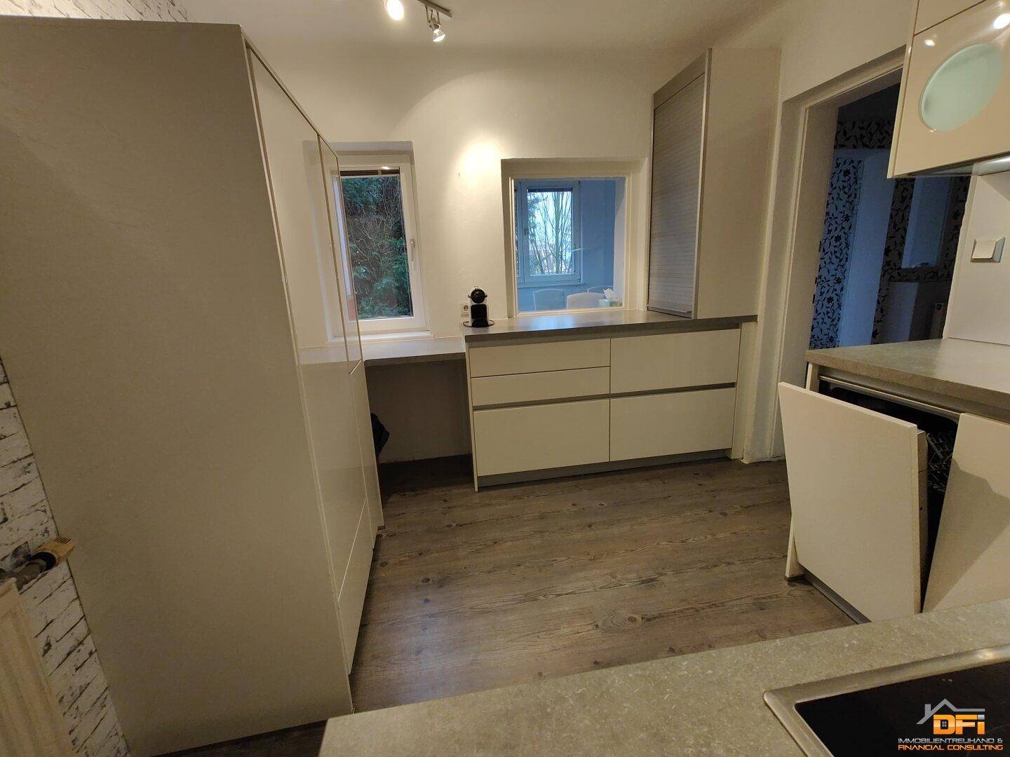 Helle Küche mit weißen Schränken, Fenstern und Blick in den Garten.