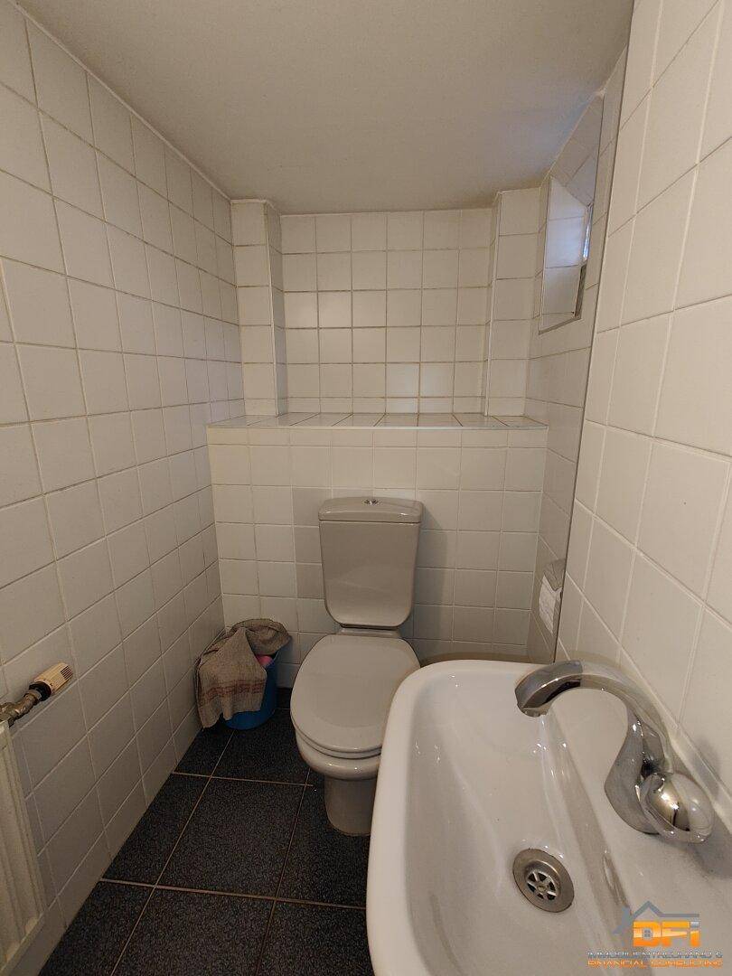 Kleines Gäste-WC mit weißen Fliesen, Toilette und Waschbecken auf dunklem Fliesenboden.