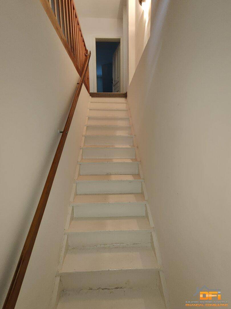 Treppenhaus mit Holzgeländer und weiß gestrichenen Stufen, führt nach oben.