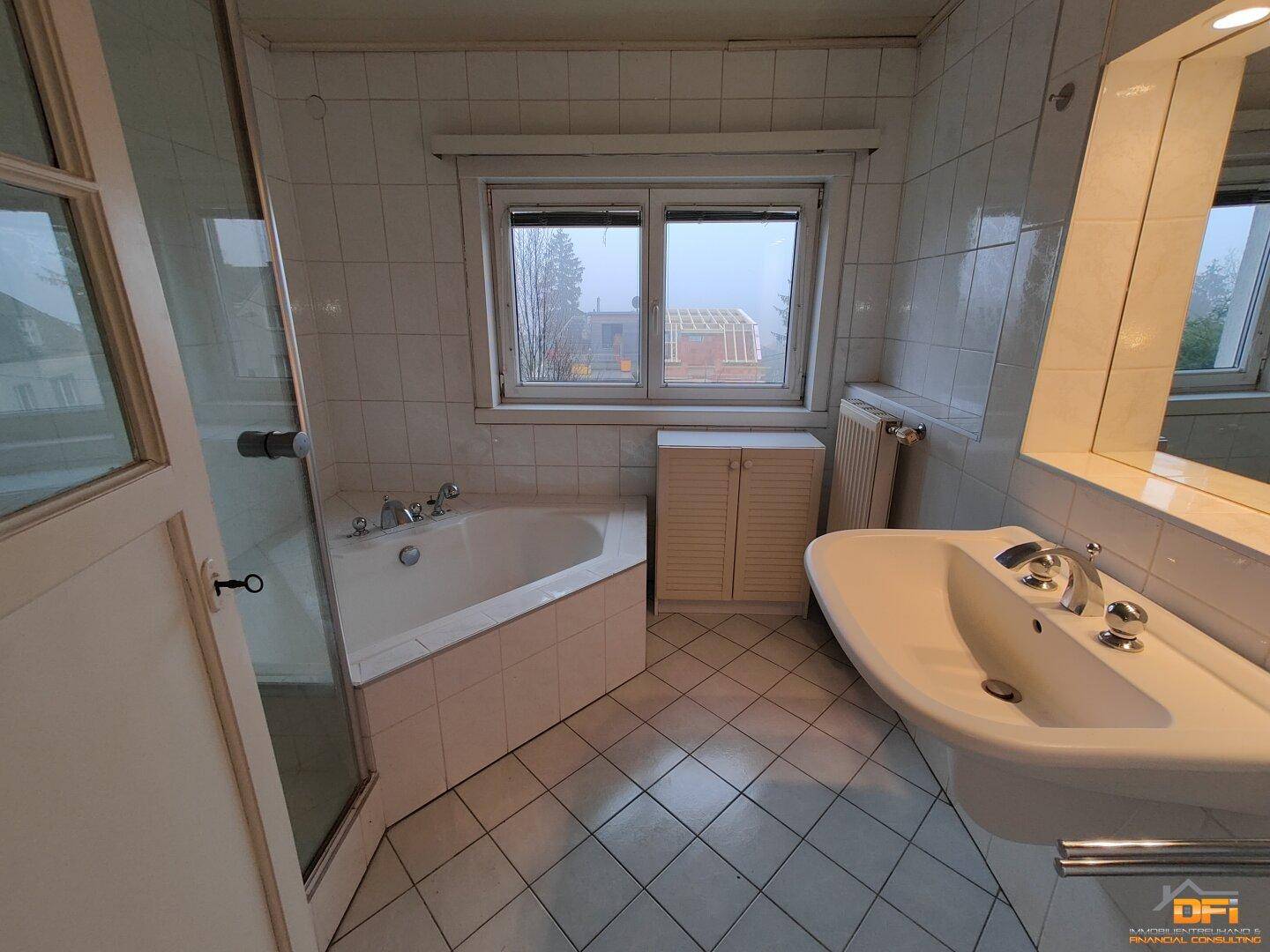 Badezimmer mit weißen Fliesen, Badewanne, Dusche und Fenster mit Ausblick.