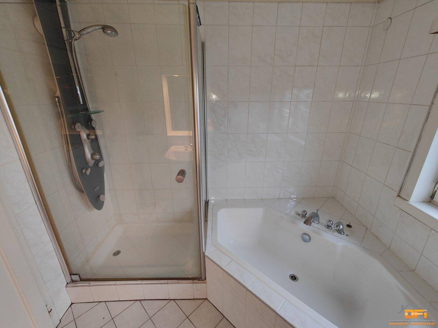 Badezimmer mit Duschkabine und Eckbadewanne, komplett mit weißen Fliesen gefliest.