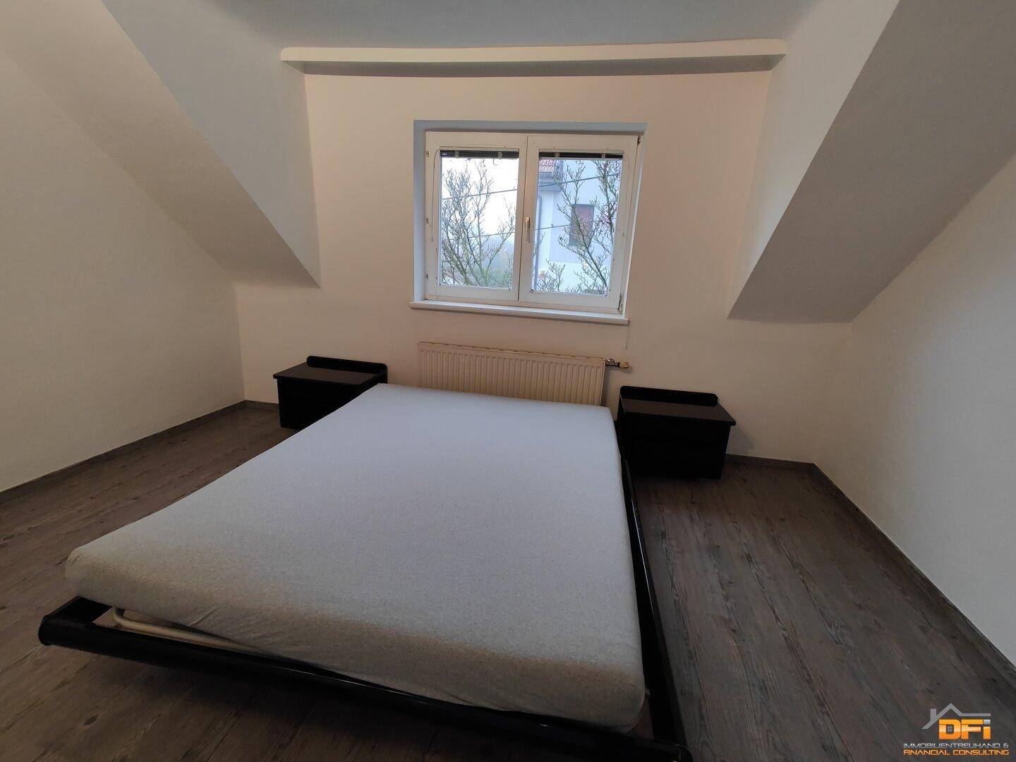Schlafzimmer mit Doppelbett, Dachschrägen und Fenster mit Ausblick auf Laminatboden.