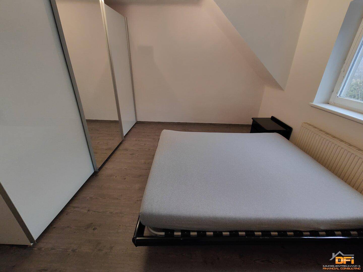 Schlafzimmer mit Doppelbett, Spiegelschrank und Dachschräge auf Laminatboden.