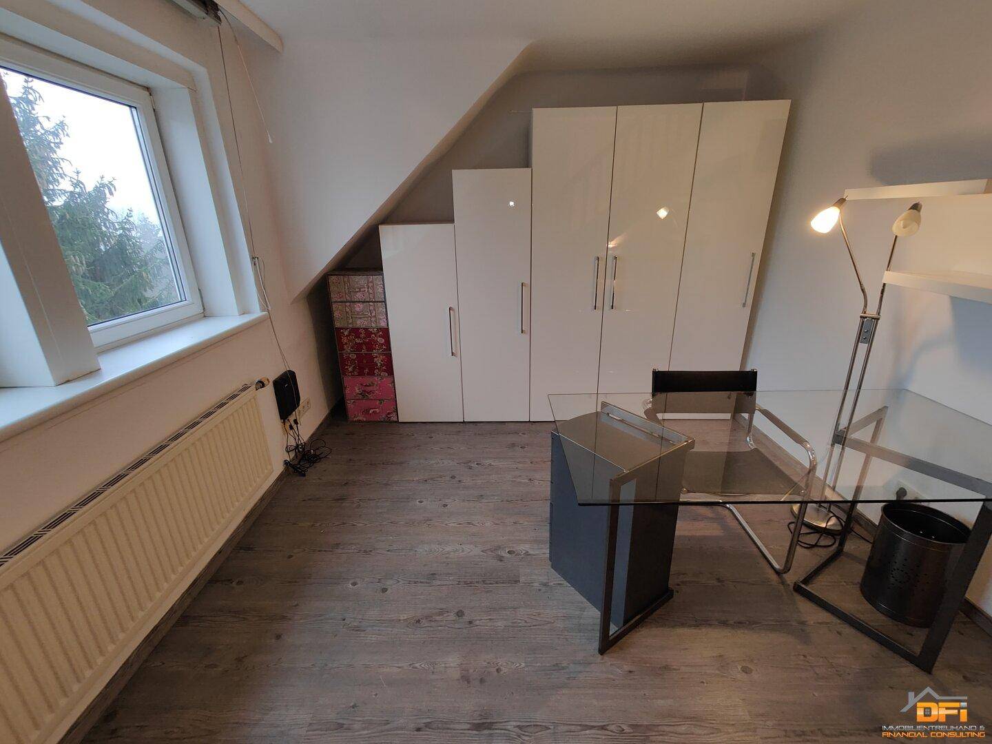 Arbeitszimmer mit Schreibtisch, Schränken und Dachschräge auf Laminatboden.