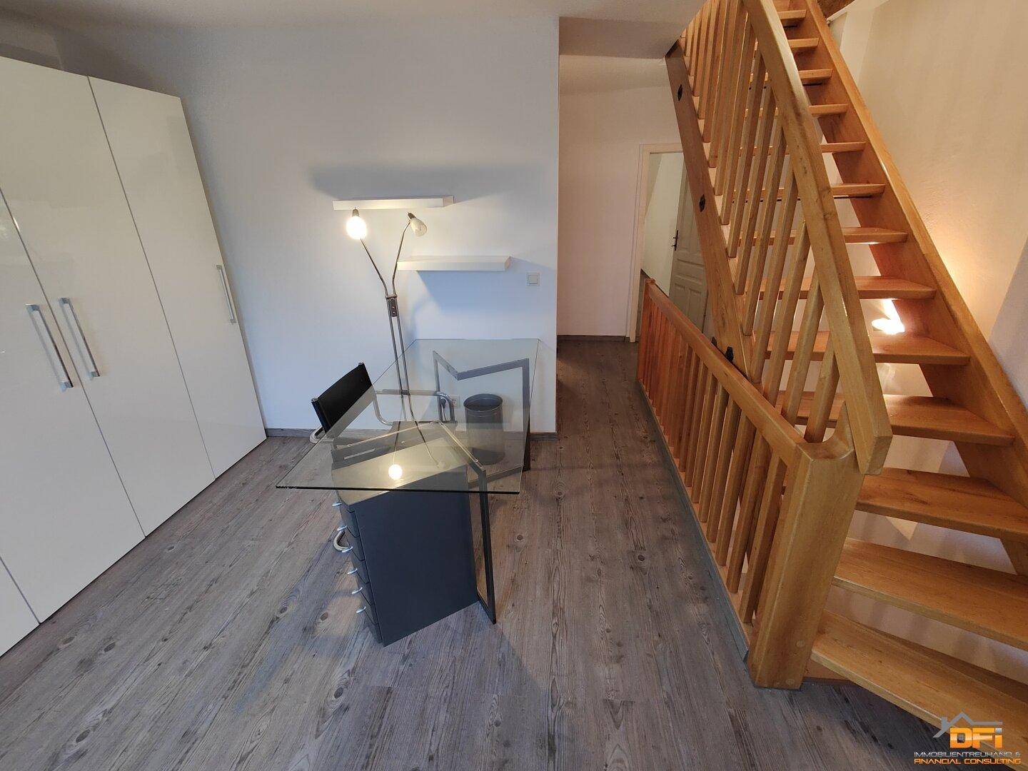 Flur mit Holztreppe und Arbeitsbereich unter der Dachschräge auf Laminatboden.