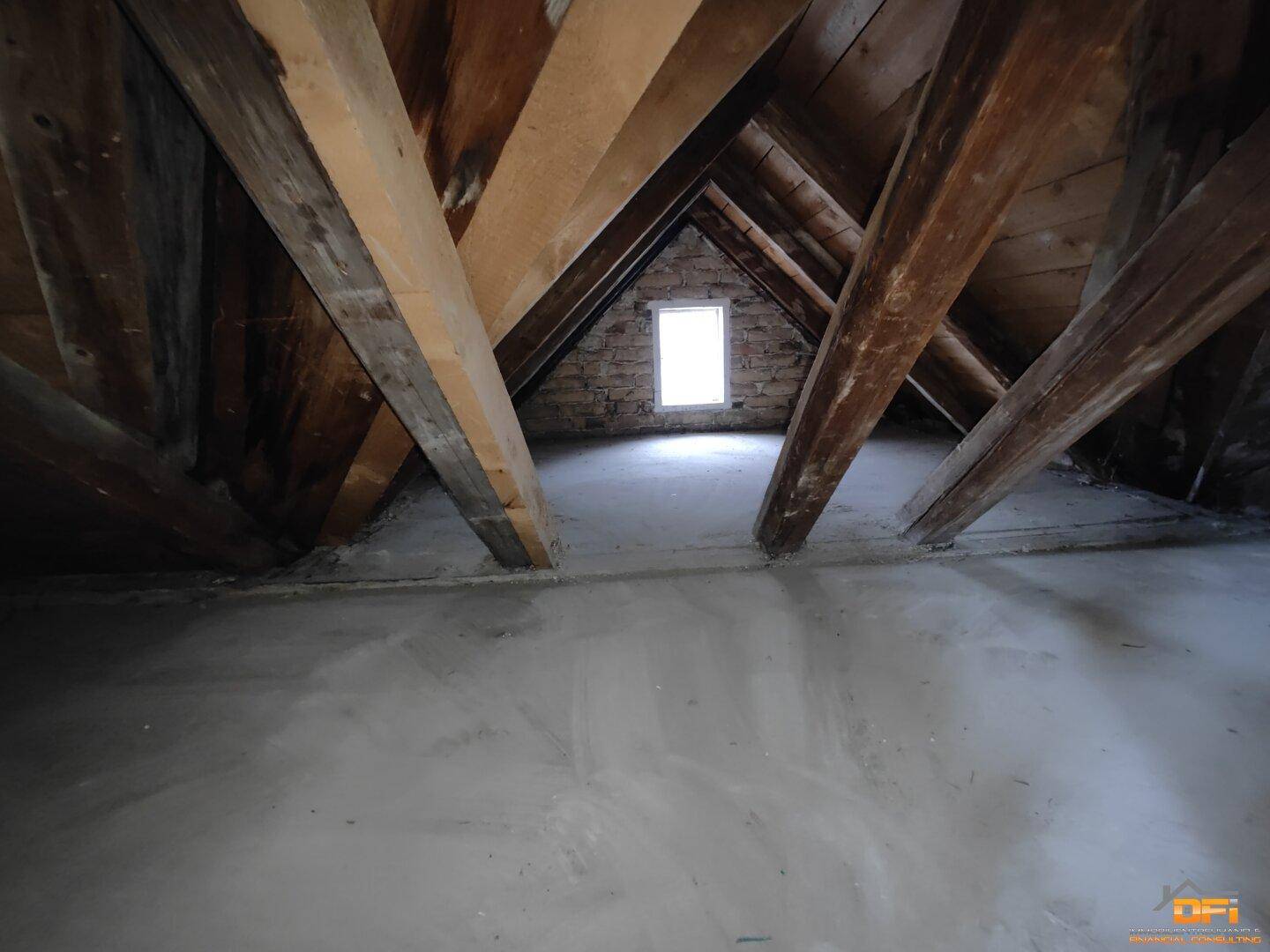Unausgebauter Dachboden mit Holzbalken und kleinem Fenster, bietet Stauraum.